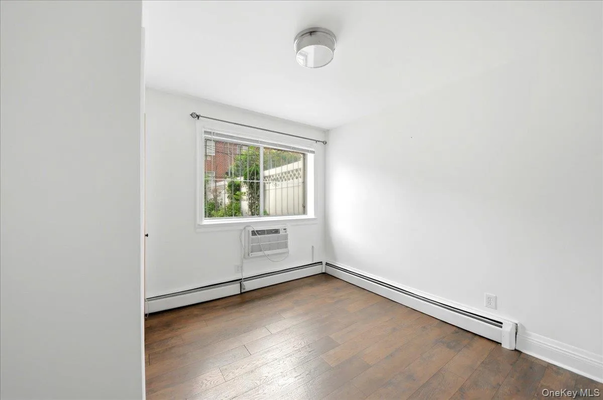 Room featuring wood-finish flooring, white walls, and a window with security bars Room featuring wood-finish flooring, white walls, and a window with security bars
