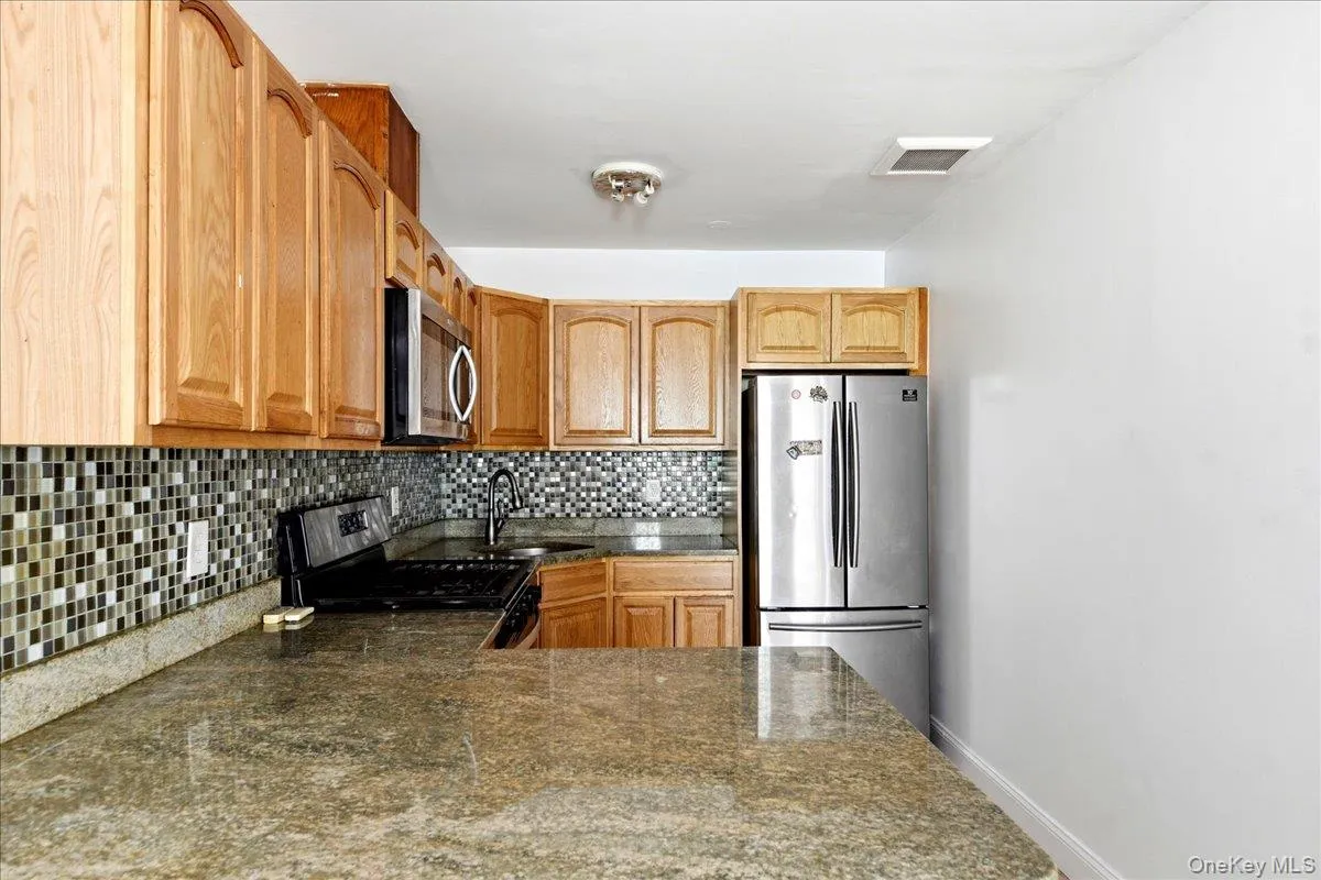 Kitchen featuring light wood cabinetry, stone countertops, mosaic tile backsplash, stainless steel appliances, and an over-range microwave Kitchen featuring light wood cabinetry, stone countertops, mosaic tile backsplash, stainless steel appliances, and an over-range microwave