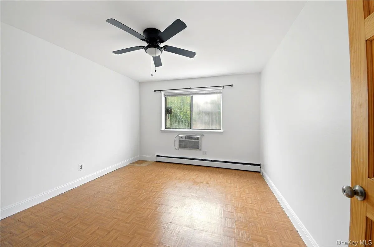 Interior room featuring parquet wood-finish flooring, white painted walls, a window unit air conditioner, and a ceiling fan with integrated lighting Interior room featuring parquet wood-finish flooring, white painted walls, a window unit air conditioner, and a ceiling fan with integrated lighting