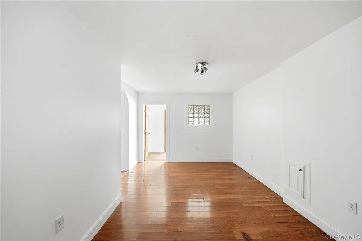 Room featuring wood-finish flooring, white walls, and a glass block window Room featuring wood-finish flooring, white walls, and a glass block window