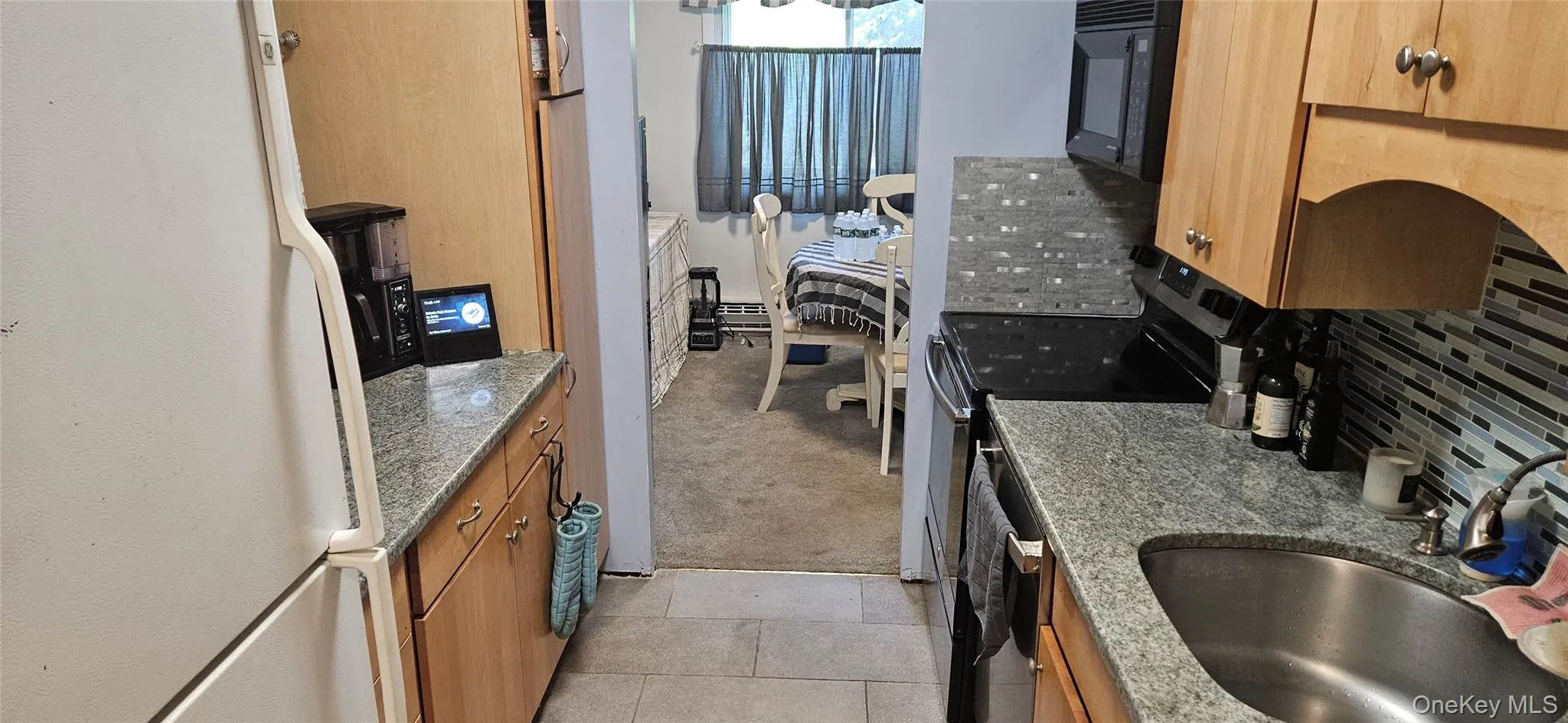 Galley kitchen featuring granite countertops, wood cabinetry, a tile backsplash, and stainless steel appliances Galley kitchen featuring granite countertops, wood cabinetry, a tile backsplash, and stainless steel appliances