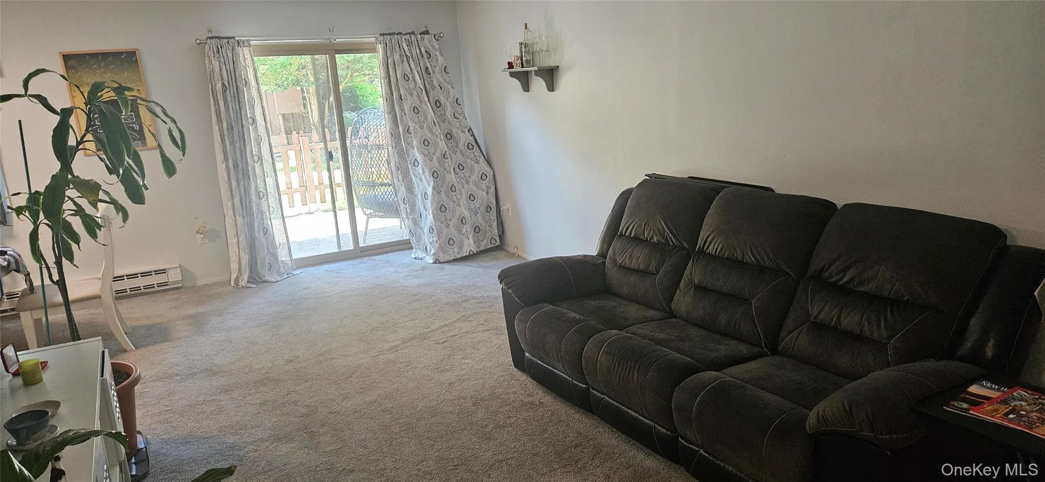 Carpeted living area featuring a sliding glass door to the exterior, white wall finishes, and a wall-mounted shelving unit Carpeted living area featuring a sliding glass door to the exterior, white wall finishes, and a wall-mounted shelving unit
