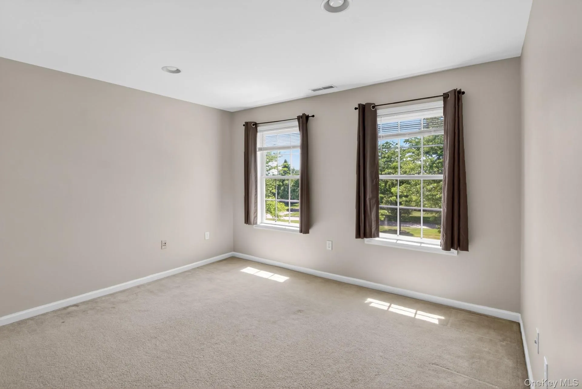 Neutral-toned carpeted room featuring two window units with white frames and brown drapes Neutral-toned carpeted room featuring two window units with white frames and brown drapes