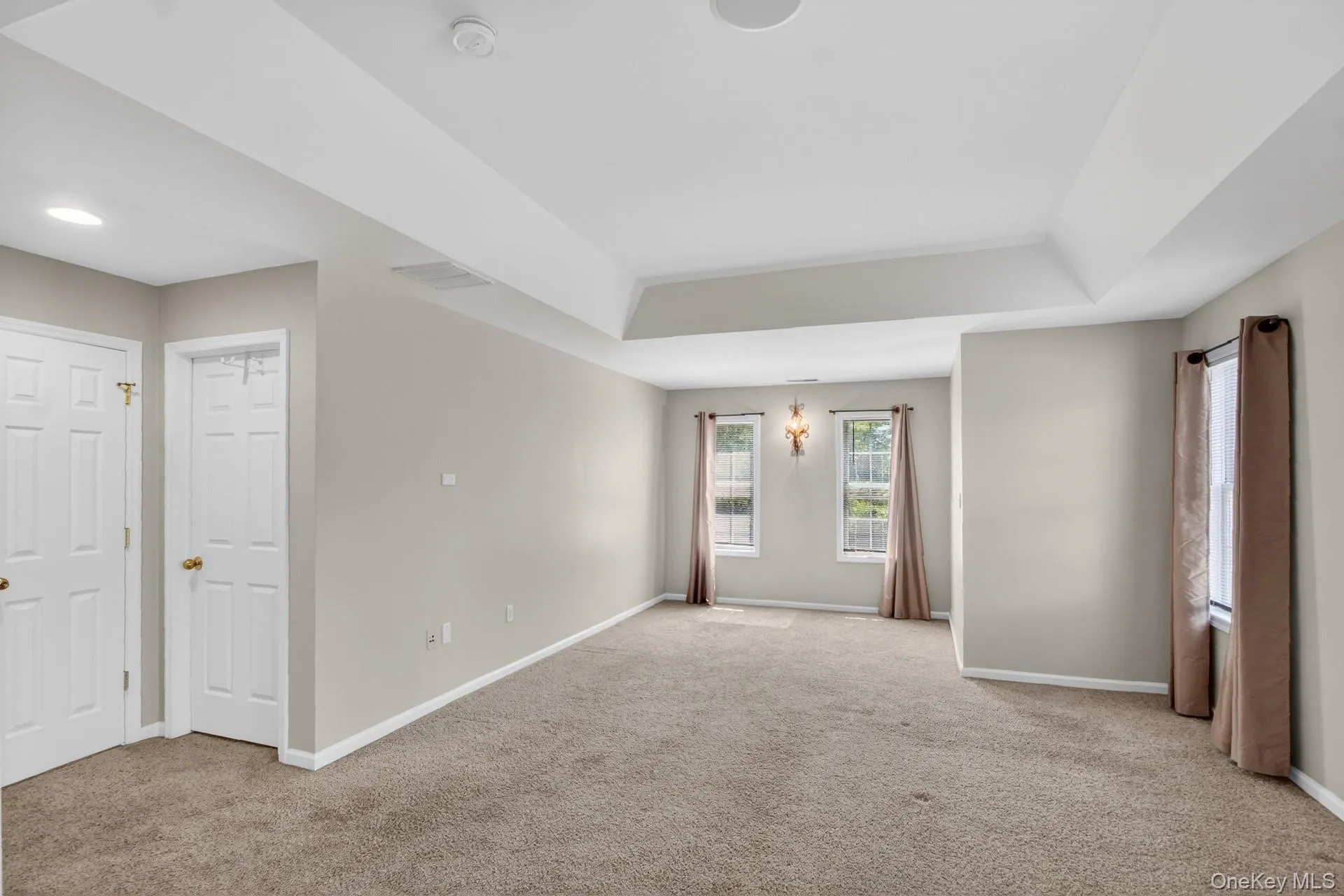 Spacious room featuring neutral carpet flooring, light-toned walls, and a multi-tiered tray ceiling Spacious room featuring neutral carpet flooring, light-toned walls, and a multi-tiered tray ceiling