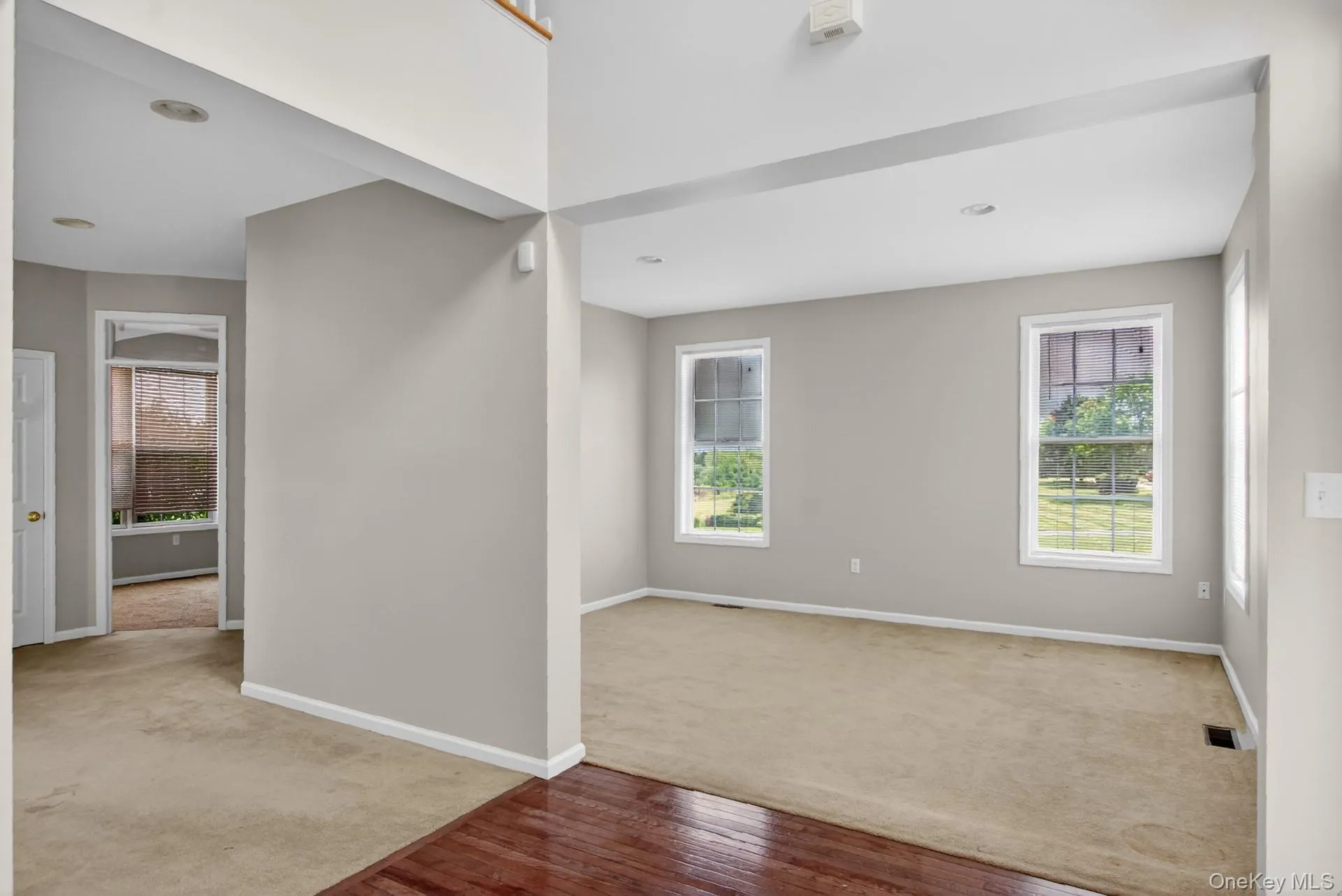 Entry foyer with wood-finish flooring opening to a carpeted room featuring two windows Entry foyer with wood-finish flooring opening to a carpeted room featuring two windows