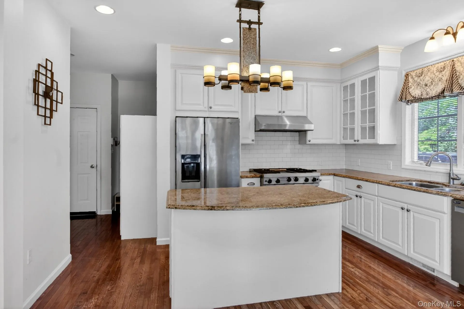 Kitchen featuring white cabinetry, stainless steel appliances, granite countertops, subway tile backsplash, and wood-finish flooring Kitchen featuring white cabinetry, stainless steel appliances, granite countertops, subway tile backsplash, and wood-finish flooring