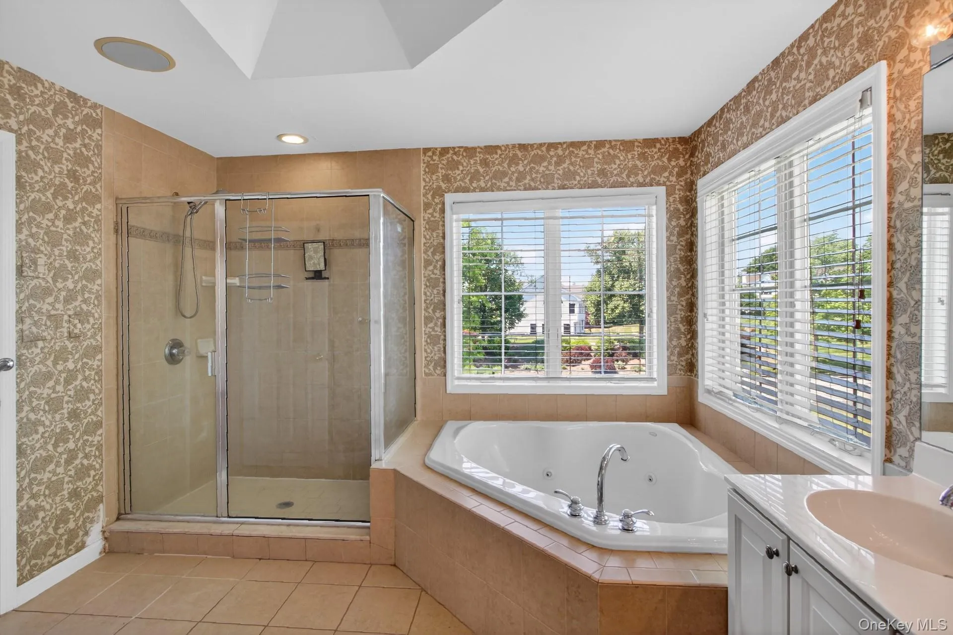 Bathroom featuring a jetted soaking tub, glass-enclosed shower, dual windows with blinds, vanity with an integrated sink, and recessed lighting Bathroom featuring a jetted soaking tub, glass-enclosed shower, dual windows with blinds, vanity with an integrated sink, and recessed lighting