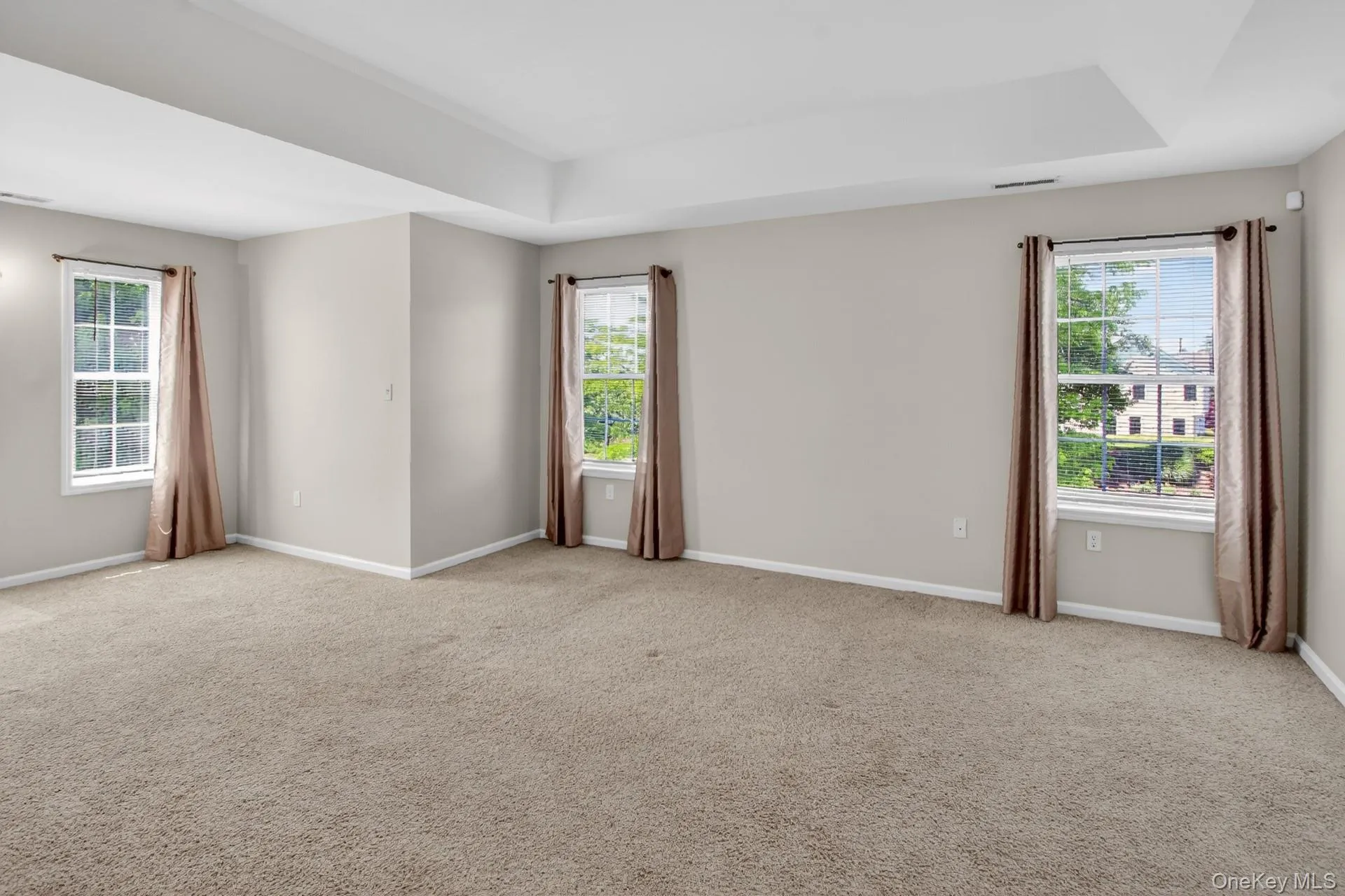 Spacious room with a neutral color palette, featuring a tray ceiling, light gray walls, and plush carpet flooring Spacious room with a neutral color palette, featuring a tray ceiling, light gray walls, and plush carpet flooring