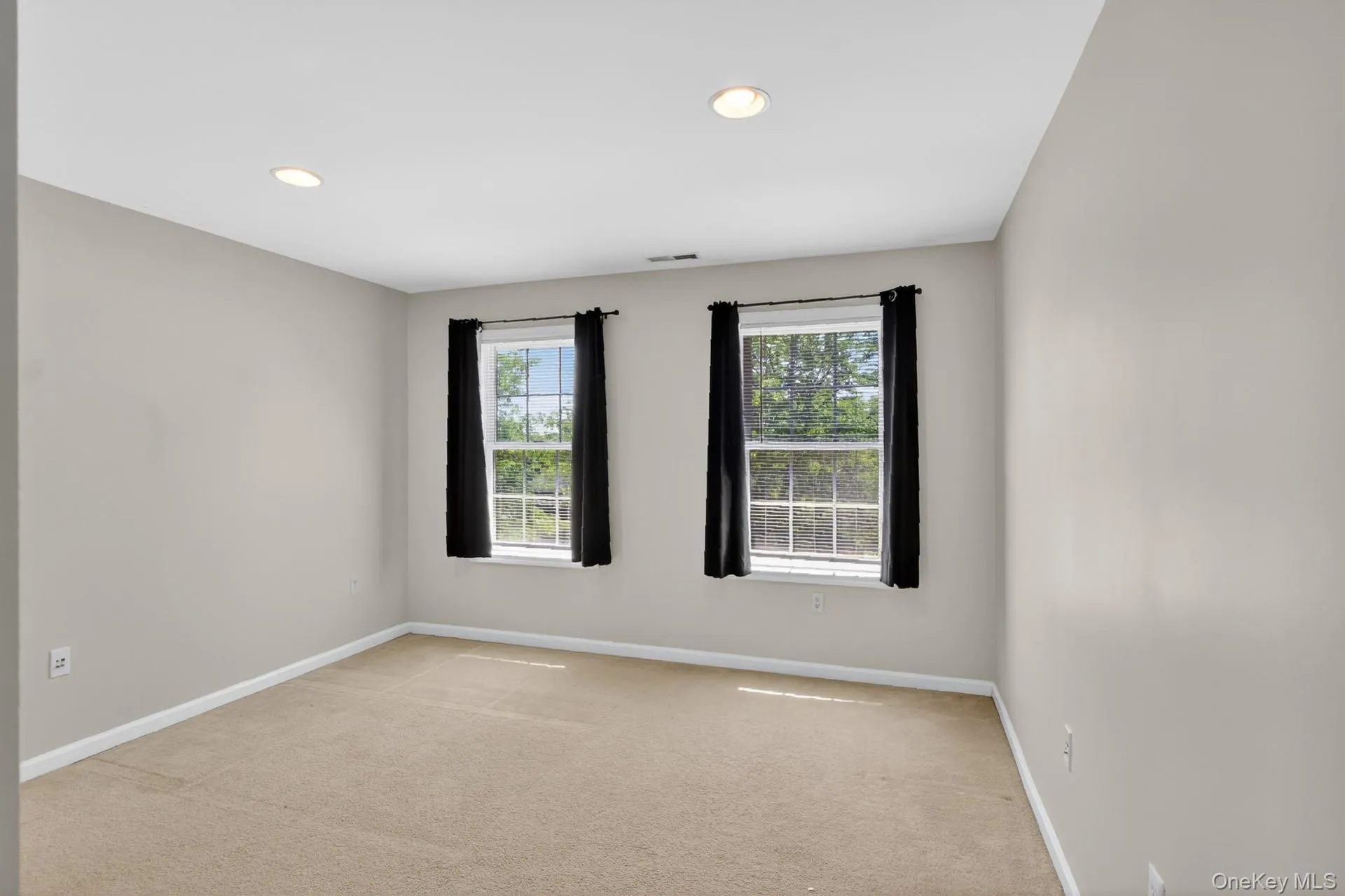 Carpeted interior room featuring two windows with dark drapes, recessed lighting, and light-toned wall paint Carpeted interior room featuring two windows with dark drapes, recessed lighting, and light-toned wall paint