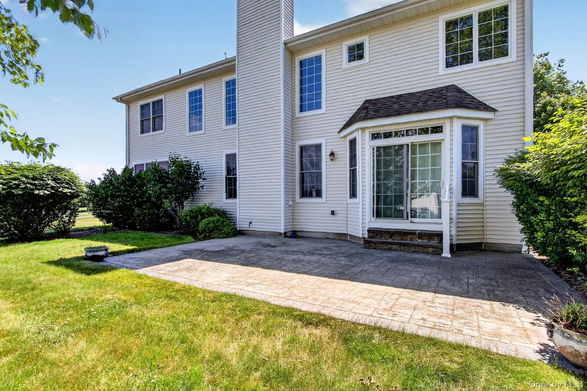 Rear exterior featuring light-colored siding, a stamped concrete patio, and a bay window with a sliding glass door Rear exterior featuring light-colored siding, a stamped concrete patio, and a bay window with a sliding glass door