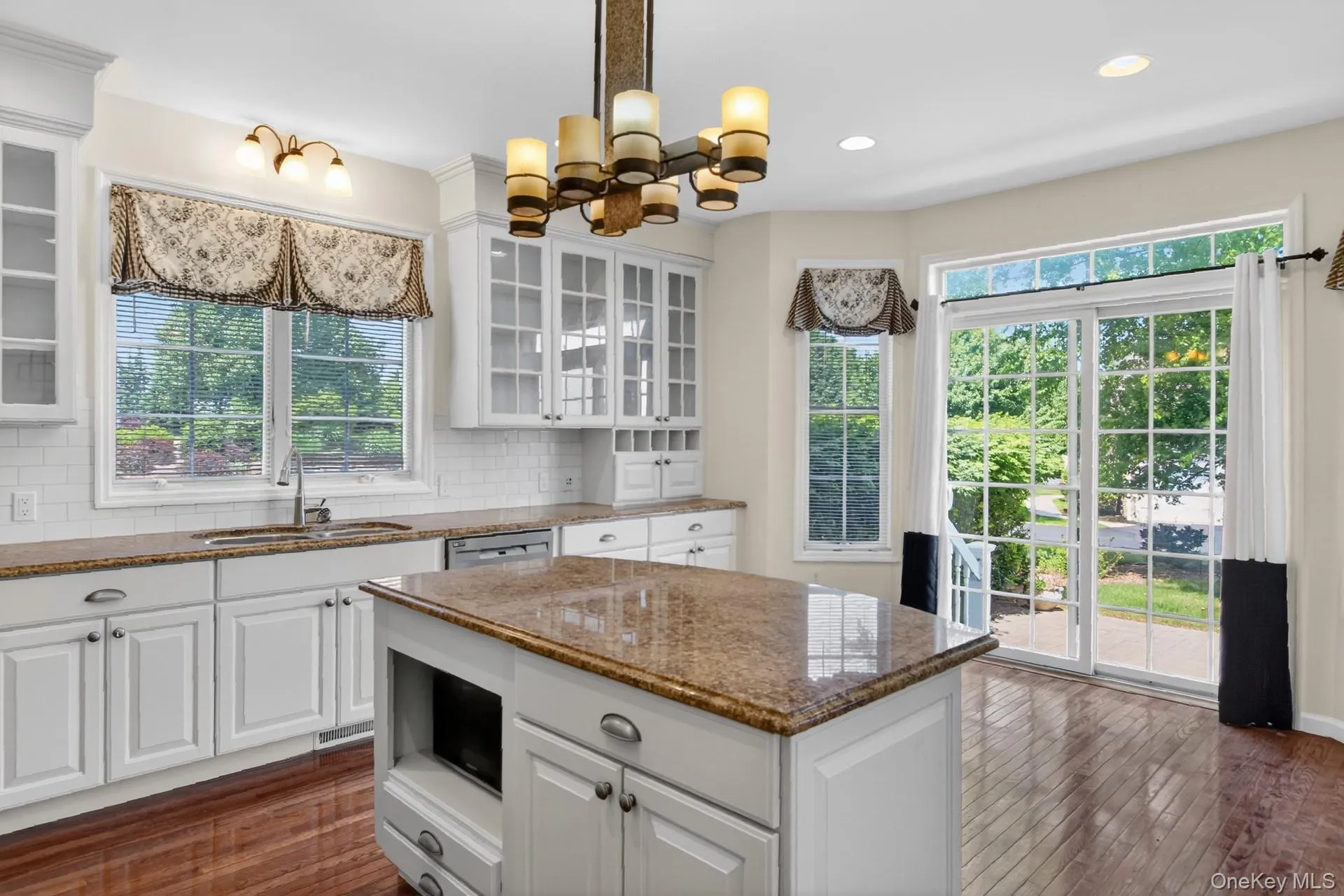 Bright kitchen featuring white cabinetry, granite countertops, a central island, wood-finish flooring, and a sliding glass door to the exterior Bright kitchen featuring white cabinetry, granite countertops, a central island, wood-finish flooring, and a sliding glass door to the exterior
