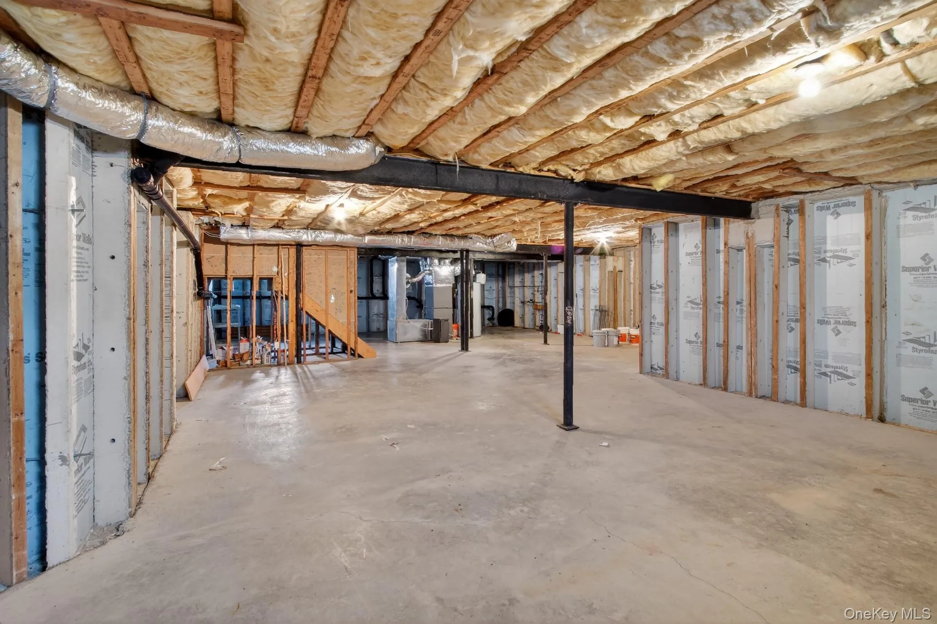 Unfinished basement featuring concrete flooring, exposed ceiling joists with insulation, and rough-in framing for future customization Unfinished basement featuring concrete flooring, exposed ceiling joists with insulation, and rough-in framing for future customization
