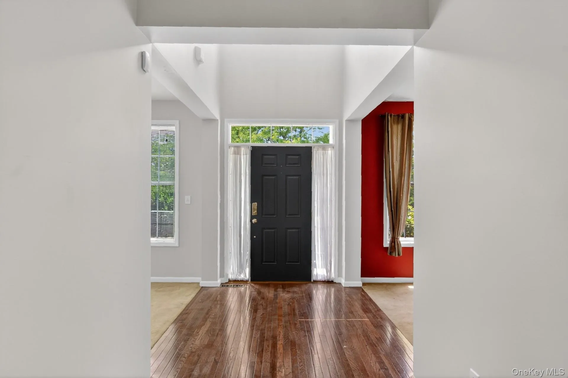 Entryway featuring high ceilings, wood-finish flooring, a dark paneled front door with transom window, and a bright interior Entryway featuring high ceilings, wood-finish flooring, a dark paneled front door with transom window, and a bright interior
