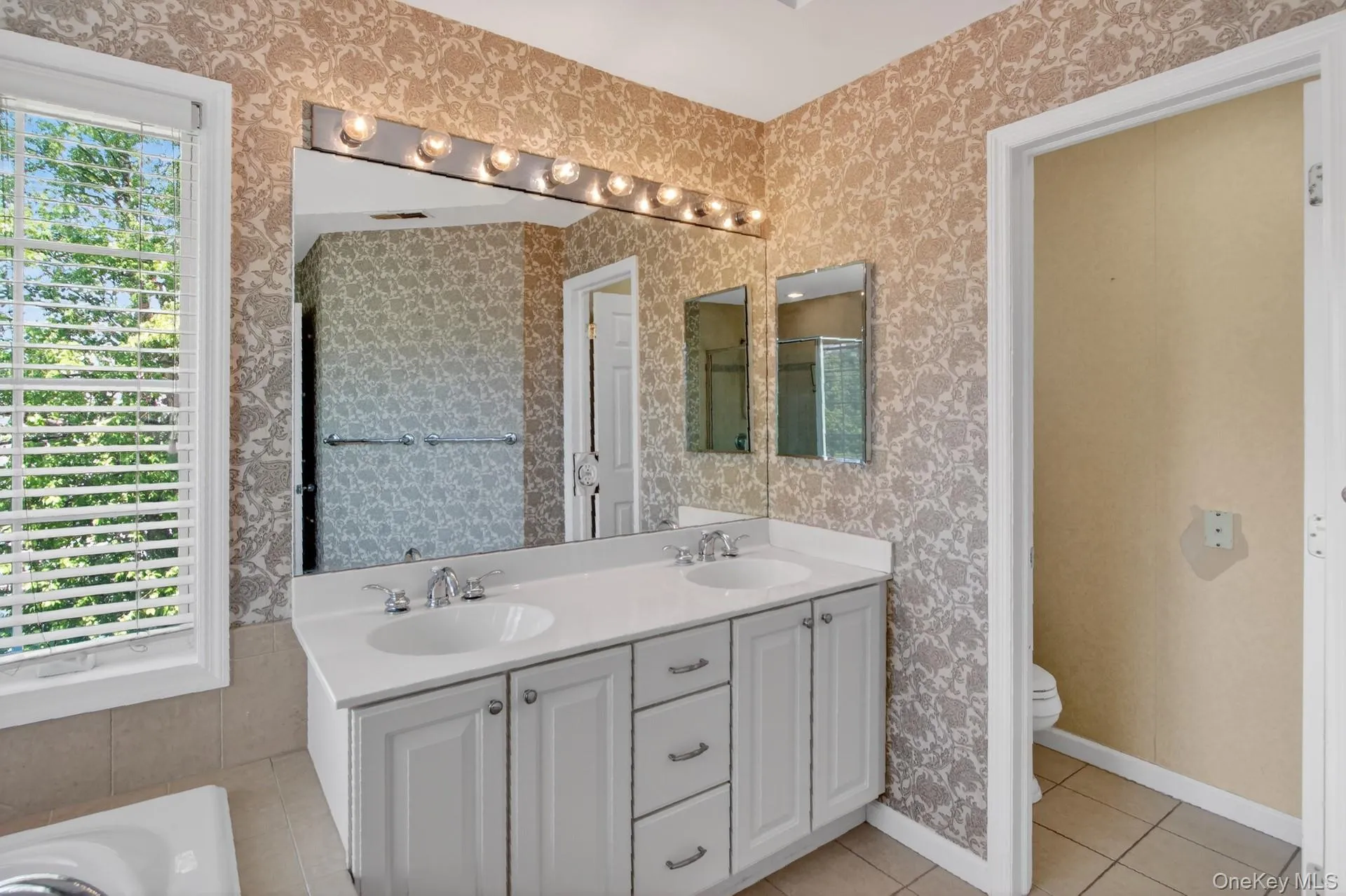 Dual vanity with white cabinetry and integrated sinks, a large wall-mounted mirror, and overhead strip lighting Dual vanity with white cabinetry and integrated sinks, a large wall-mounted mirror, and overhead strip lighting