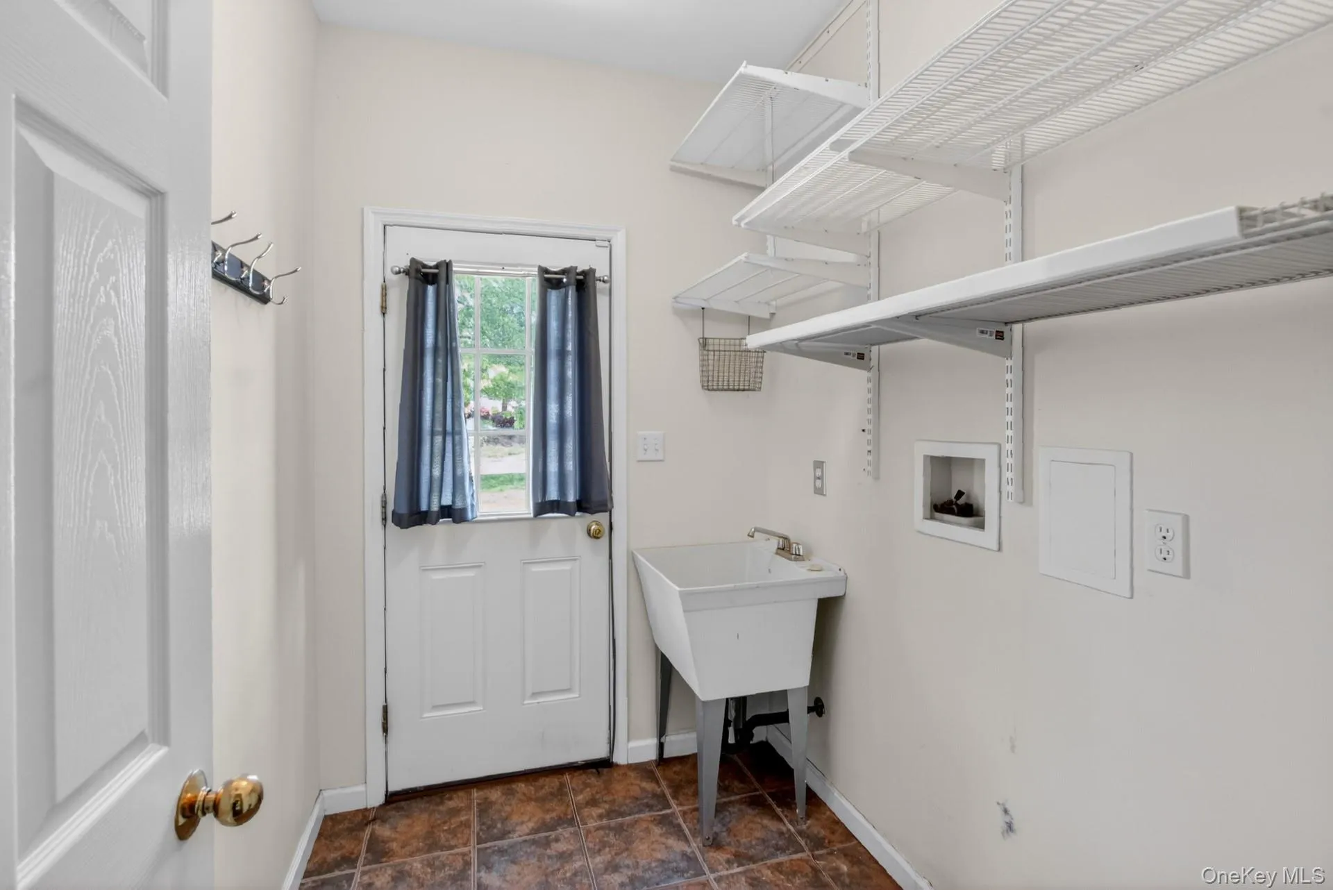 Utility room featuring a white door with transom window, a utility sink, and wall-mounted shelving Utility room featuring a white door with transom window, a utility sink, and wall-mounted shelving