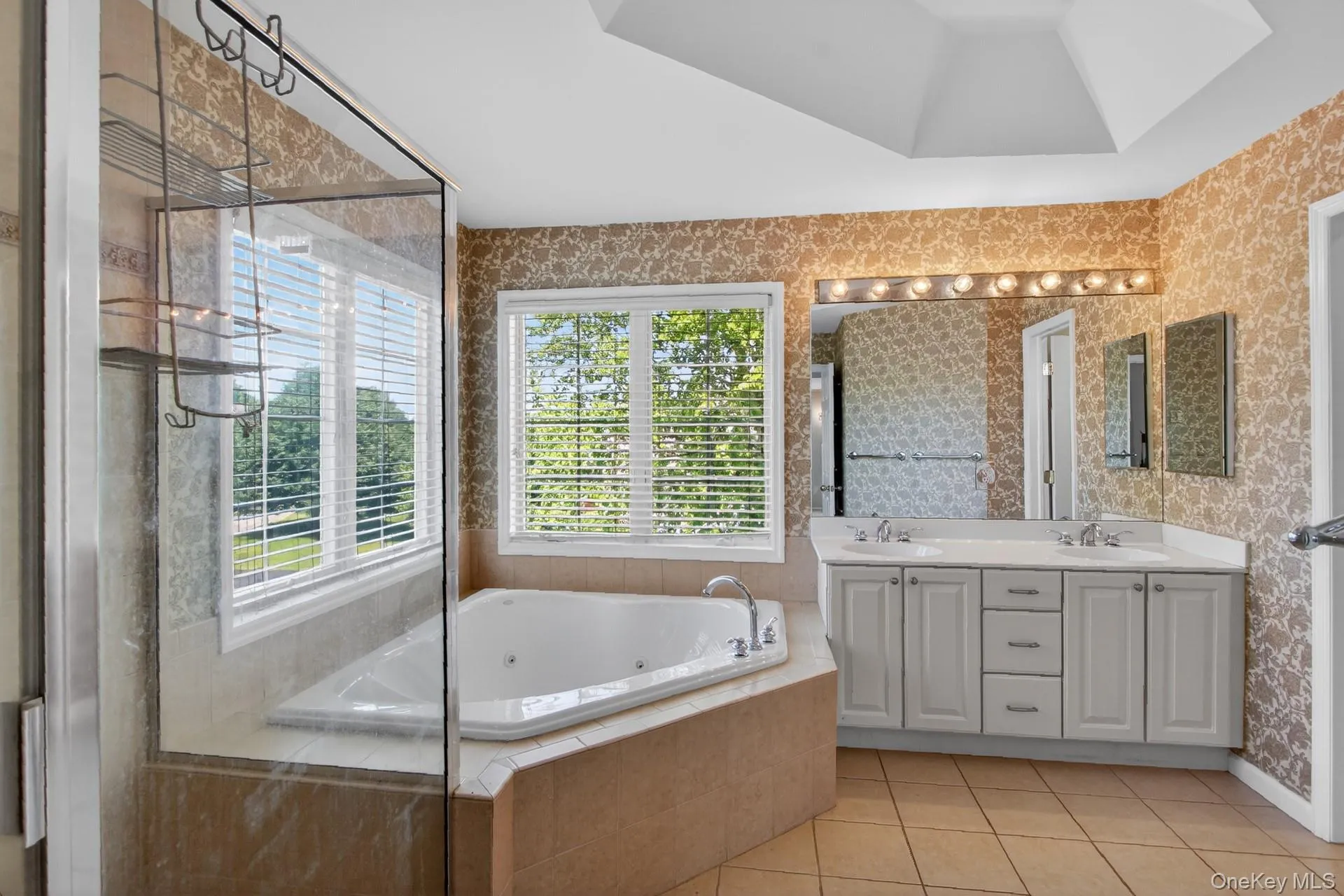 Recessed jetted tub with tile surround, double vanity with dual sinks, mirrored wall, and glass-enclosed shower Recessed jetted tub with tile surround, double vanity with dual sinks, mirrored wall, and glass-enclosed shower