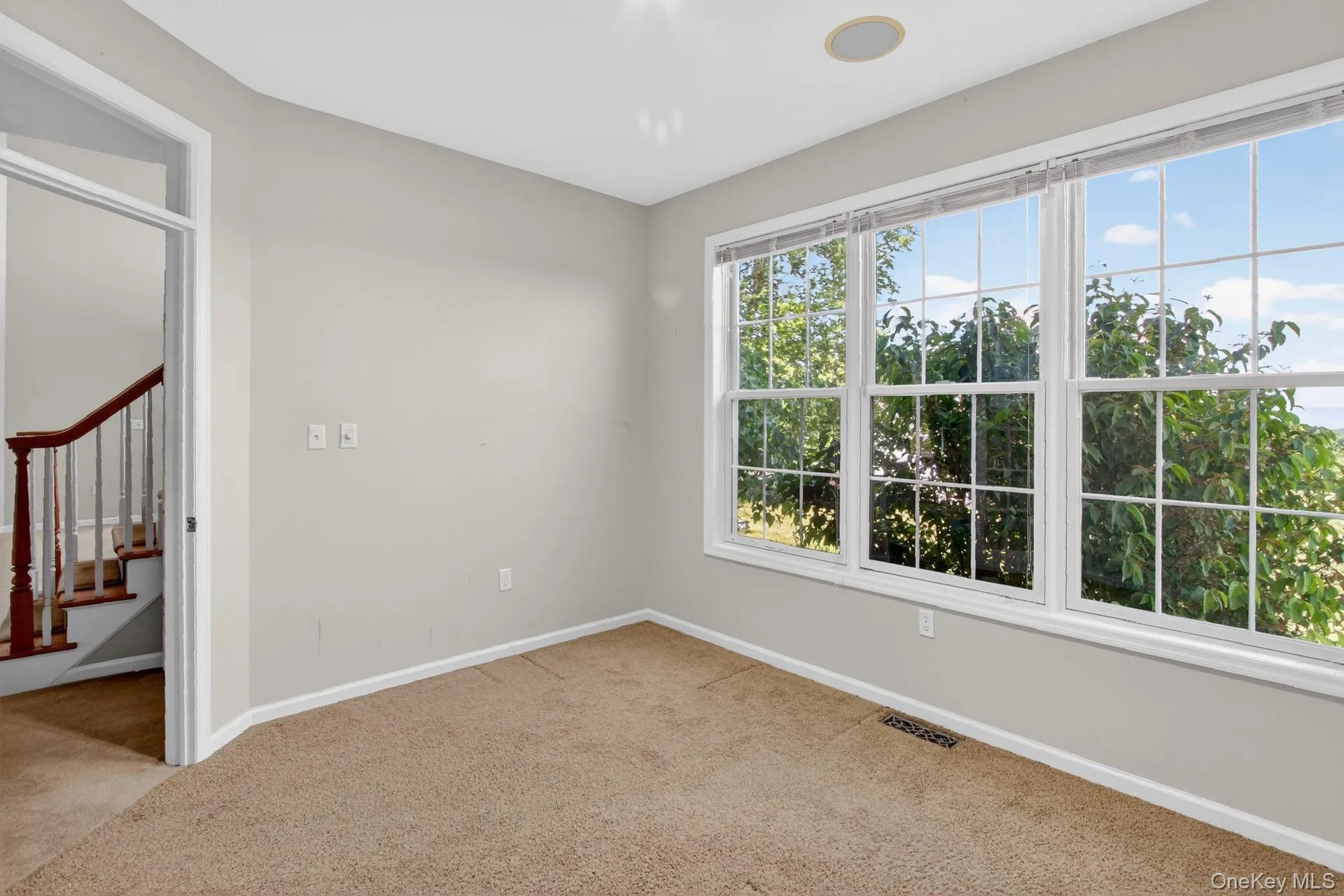 Bright interior room with extensive multi-panel windows, light neutral wall paint, and a built-in ceiling speaker Bright interior room with extensive multi-panel windows, light neutral wall paint, and a built-in ceiling speaker