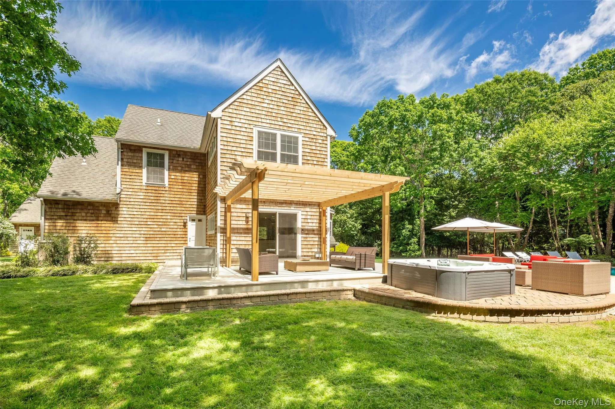 Rear exterior featuring cedar shake siding, a multi-level patio, a wooden pergola, a hot tub, and a brick paver surround Rear exterior featuring cedar shake siding, a multi-level patio, a wooden pergola, a hot tub, and a brick paver surround