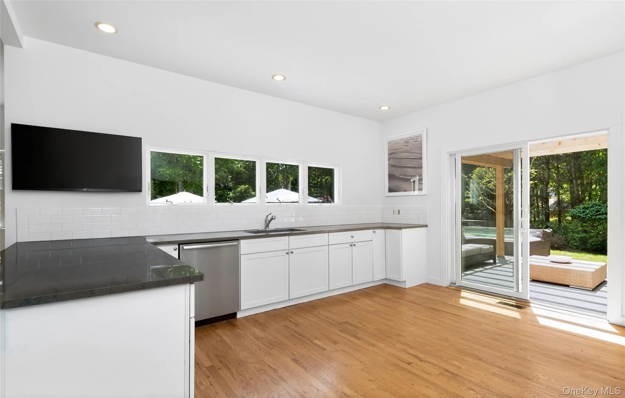 Kitchen space featuring light wood-finish flooring, white cabinetry, dark countertops, and a white subway tile backsplash Kitchen space featuring light wood-finish flooring, white cabinetry, dark countertops, and a white subway tile backsplash