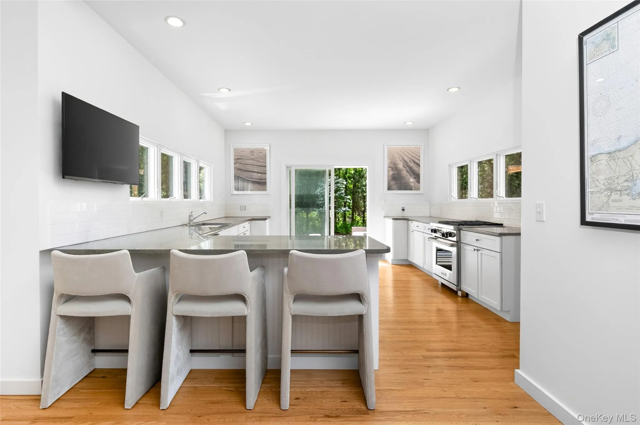 Spacious kitchen featuring an extended island with counter seating, stainless steel appliances, abundant white cabinetry, white subway tile backsplash, and wood-finish flooring Spacious kitchen featuring an extended island with counter seating, stainless steel appliances, abundant white cabinetry, white subway tile backsplash, and wood-finish flooring