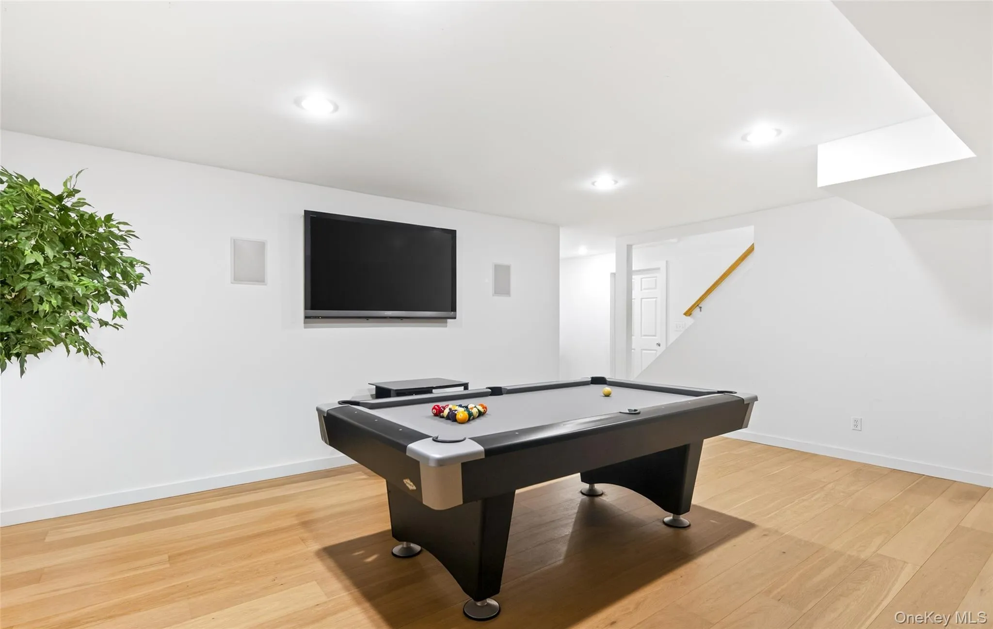Recreation room featuring wood-finish flooring, recessed lighting, and a wall-mounted flat-screen display Recreation room featuring wood-finish flooring, recessed lighting, and a wall-mounted flat-screen display