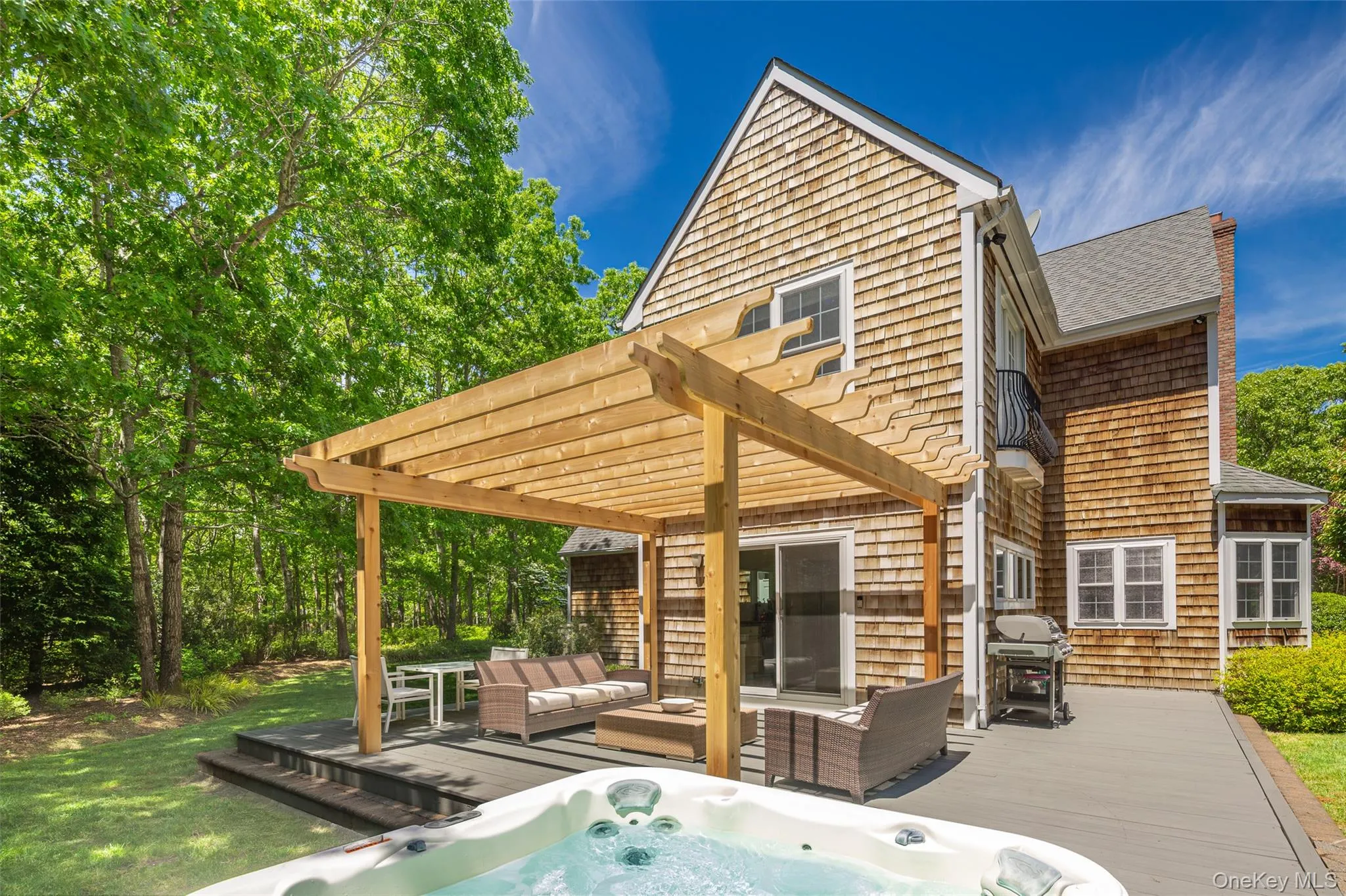 Expansive outdoor living area featuring a hot tub, a composite deck with built-in steps, and a wooden pergola Expansive outdoor living area featuring a hot tub, a composite deck with built-in steps, and a wooden pergola