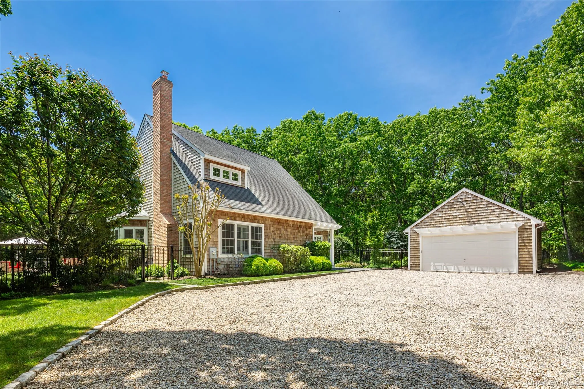 Gravel driveway leading to a shingle-sided residence with a prominent brick chimney, dormer window, and an accompanying detached garage Gravel driveway leading to a shingle-sided residence with a prominent brick chimney, dormer window, and an accompanying detached garage