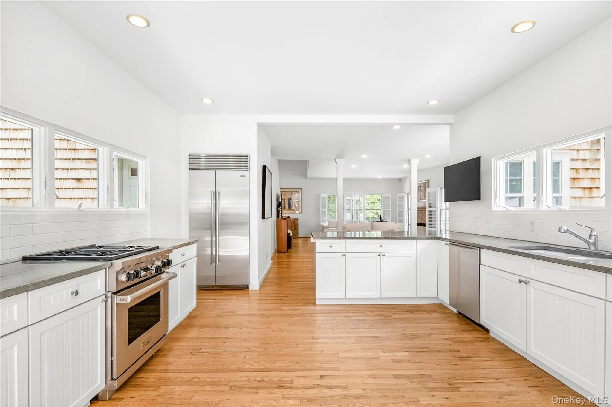 Contemporary kitchen featuring hardwood flooring, white cabinetry, integrated stainless steel appliances, and recessed lighting Contemporary kitchen featuring hardwood flooring, white cabinetry, integrated stainless steel appliances, and recessed lighting
