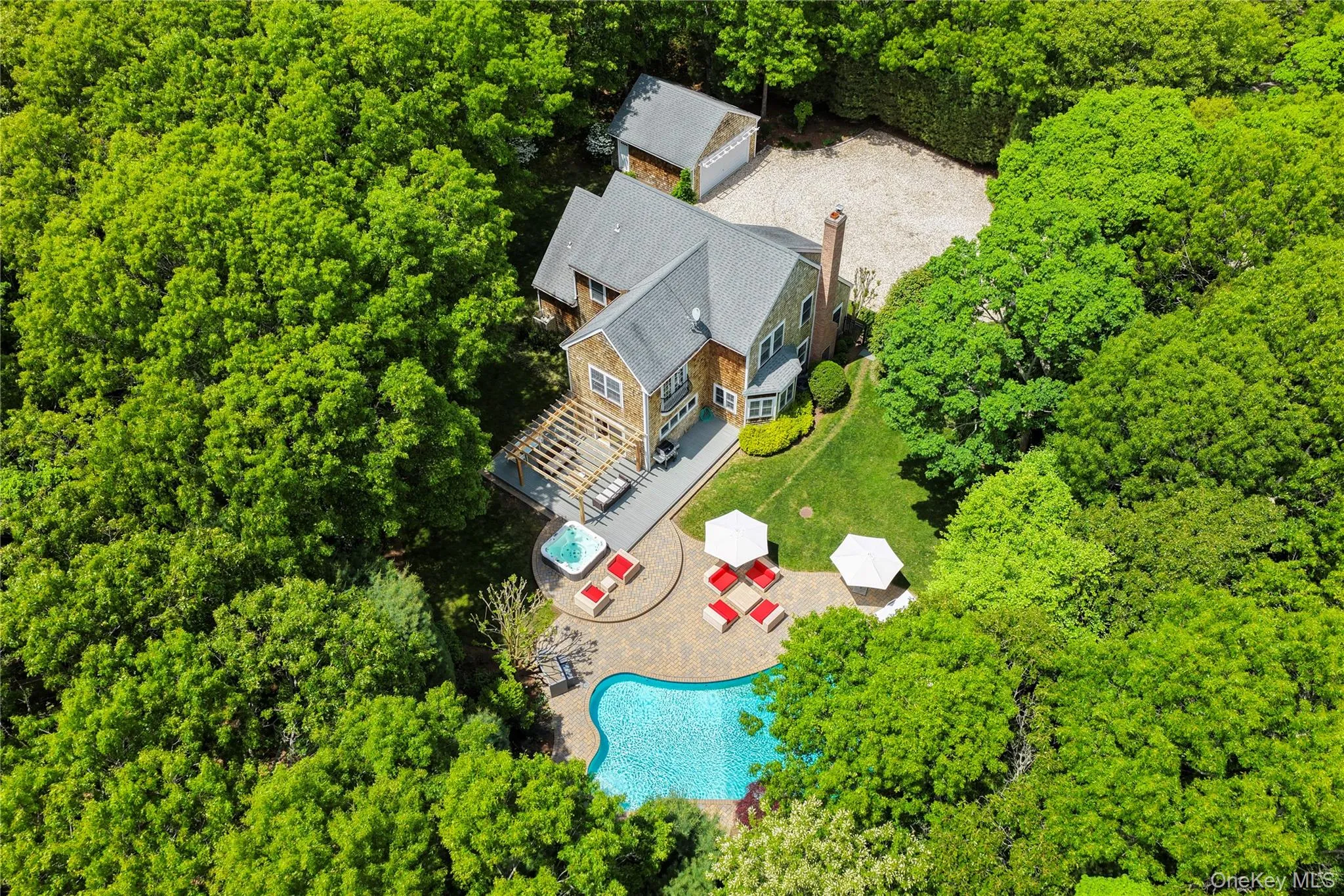 Shingle-sided residence surrounded by mature trees, featuring a gabled roof and a brick chimney Shingle-sided residence surrounded by mature trees, featuring a gabled roof and a brick chimney