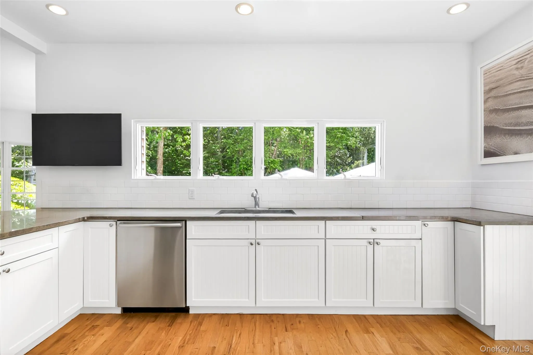 Modern kitchen featuring white cabinetry, a stainless steel dishwasher, a single basin sink, and a light-toned countertop Modern kitchen featuring white cabinetry, a stainless steel dishwasher, a single basin sink, and a light-toned countertop