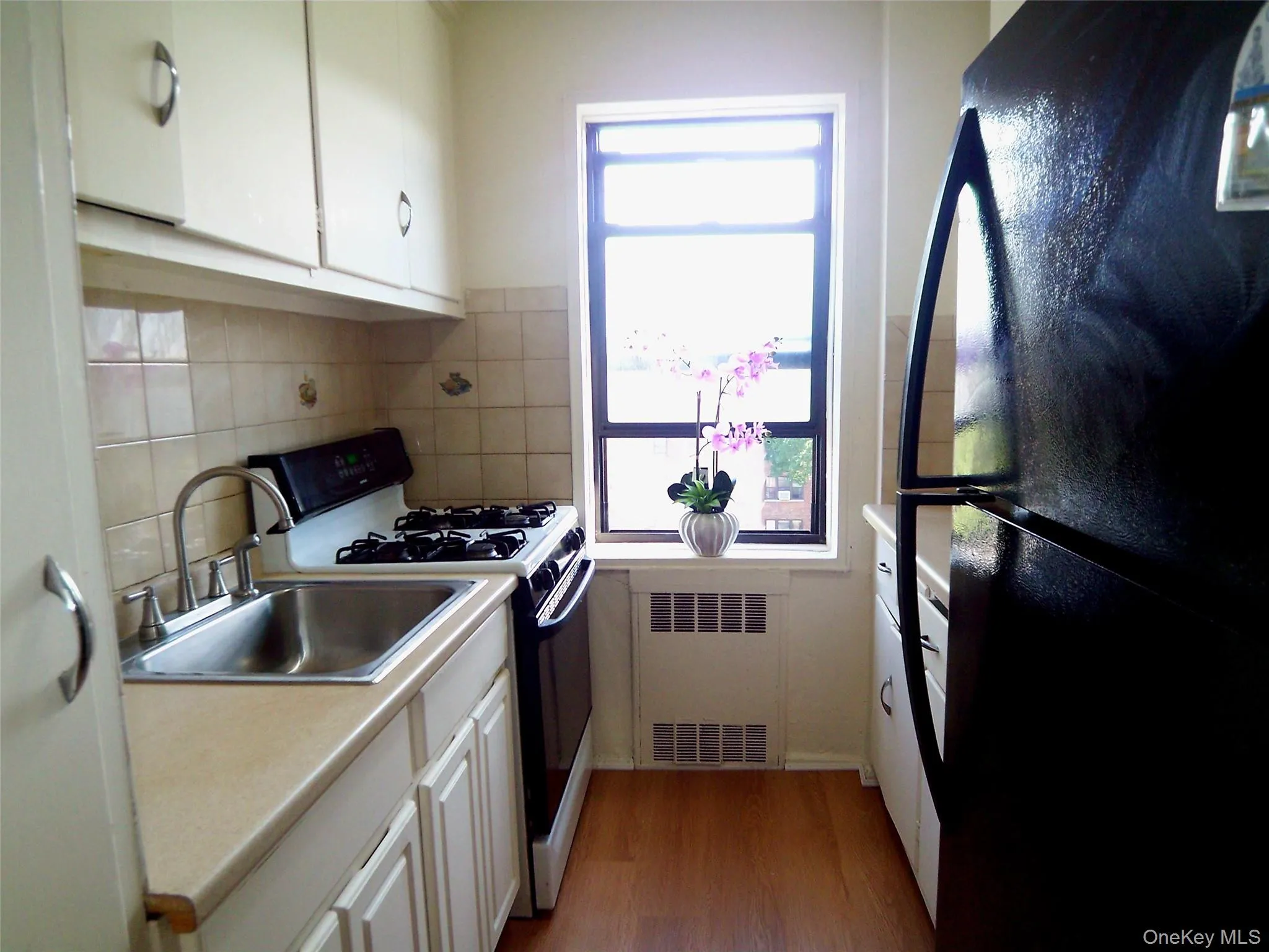 Compact kitchen featuring a stainless steel sink, gas range, wood-finish flooring, and white cabinetry Compact kitchen featuring a stainless steel sink, gas range, wood-finish flooring, and white cabinetry