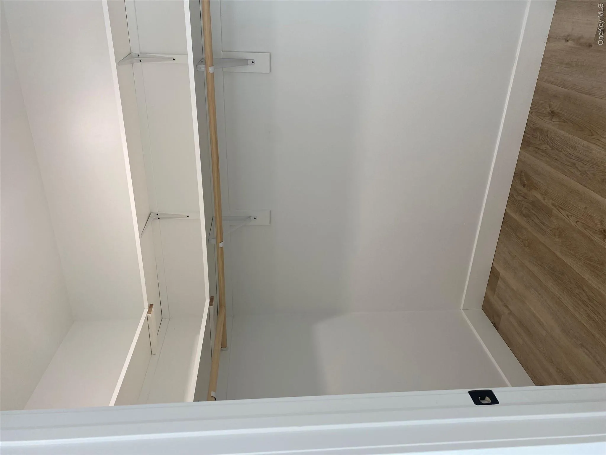 Walk-in closet featuring wood-finish flooring, white baseboards, and built-in white shelving with hanging rods Walk-in closet featuring wood-finish flooring, white baseboards, and built-in white shelving with hanging rods