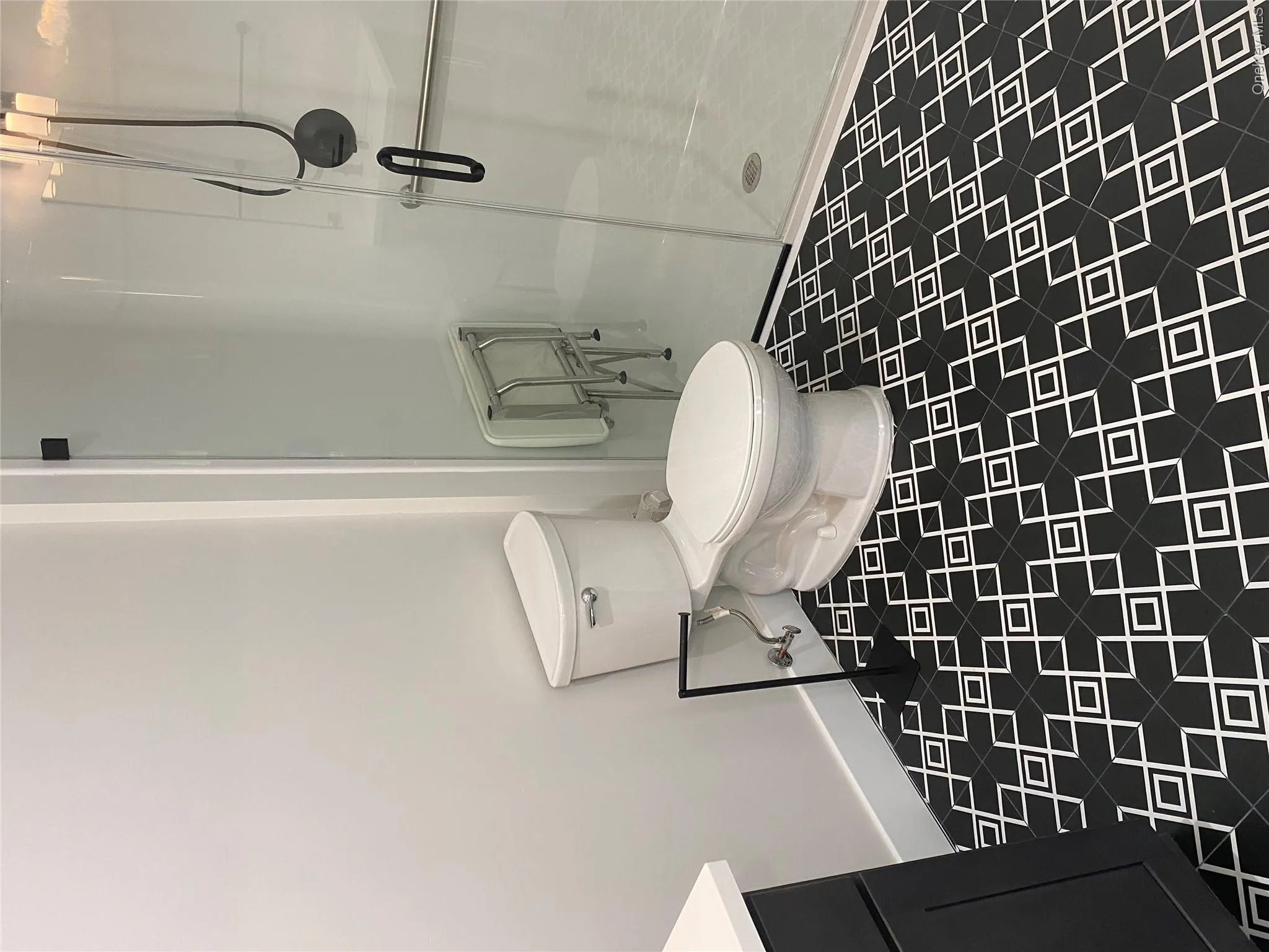 Bathroom featuring black and white patterned floor tiles, a glass-enclosed shower with black hardware, and a white toilet Bathroom featuring black and white patterned floor tiles, a glass-enclosed shower with black hardware, and a white toilet