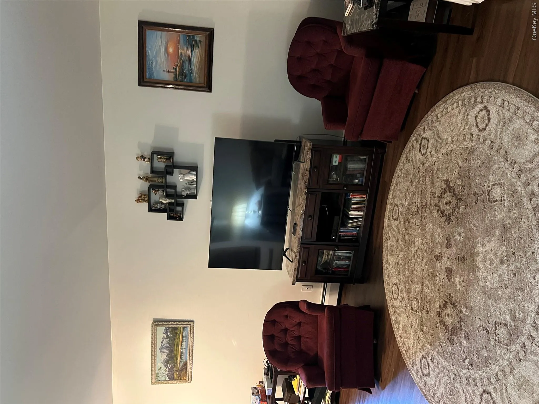 Spacious room featuring wood-finish flooring, light-toned wall paint, and a dark wood media console with a stone-look top Spacious room featuring wood-finish flooring, light-toned wall paint, and a dark wood media console with a stone-look top