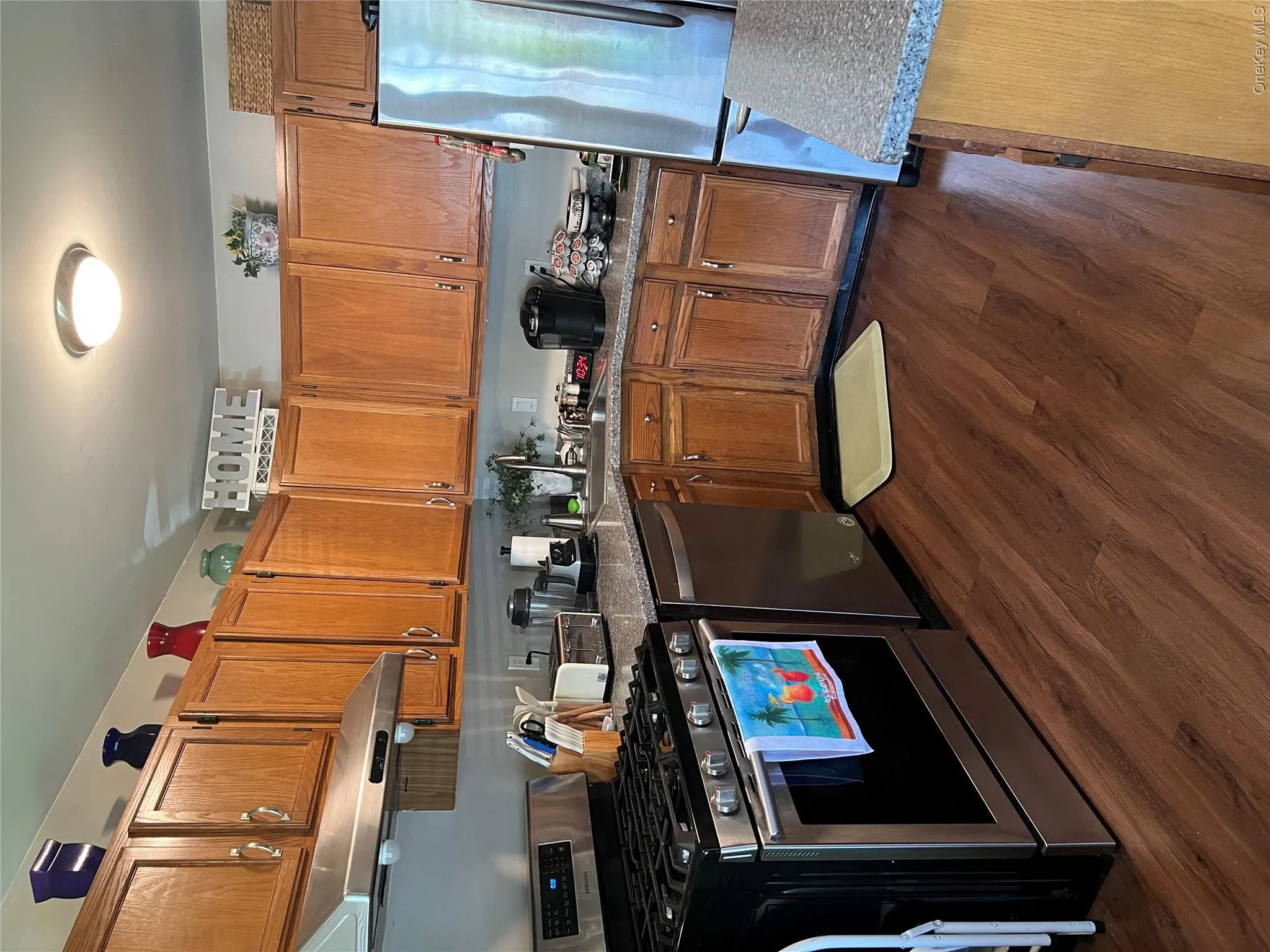 Kitchen featuring wood-finish flooring, natural wood cabinetry, stainless steel appliances, and solid surface countertops Kitchen featuring wood-finish flooring, natural wood cabinetry, stainless steel appliances, and solid surface countertops