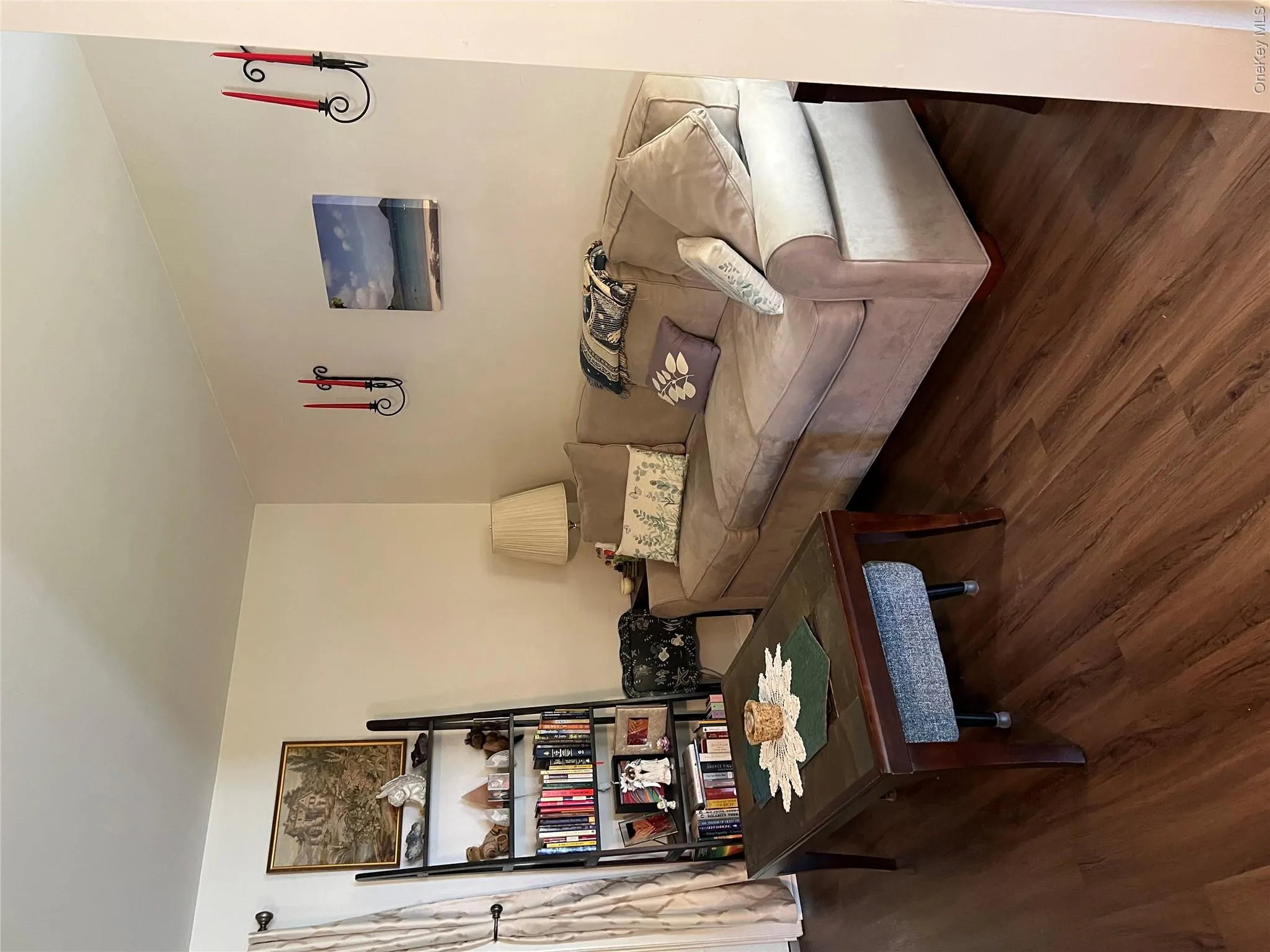 Warm living space featuring wood-finish flooring, white walls, and a window with curtain rod and drapes Warm living space featuring wood-finish flooring, white walls, and a window with curtain rod and drapes