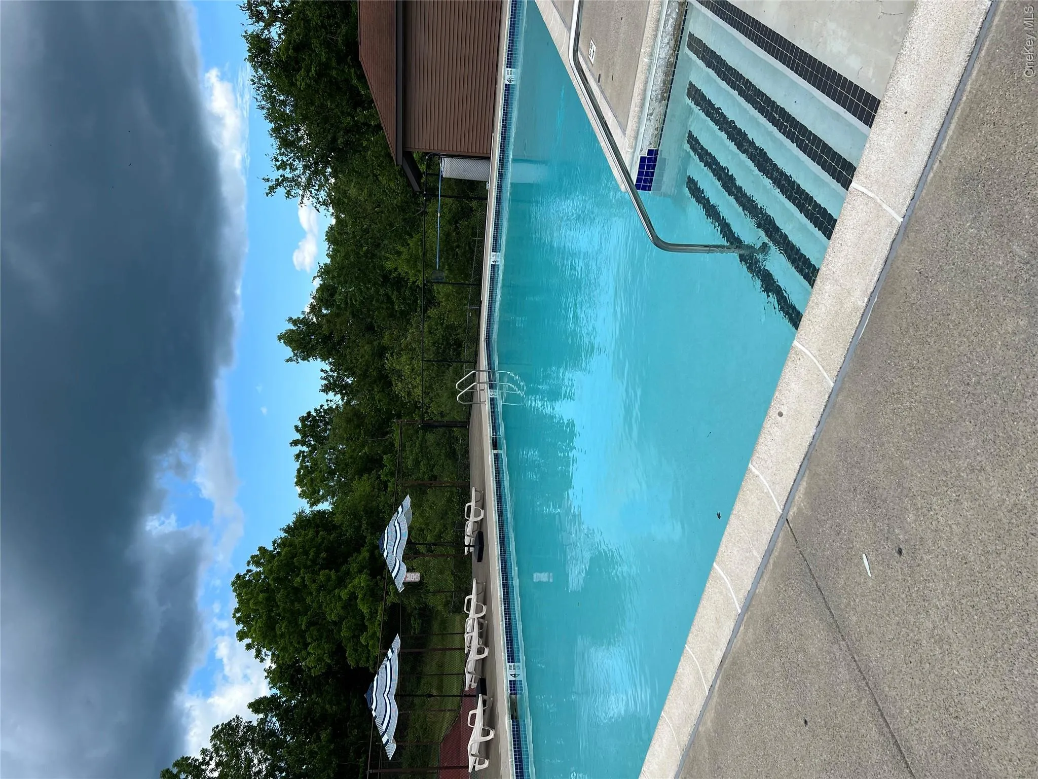 Sparkling blue swimming pool featuring integrated steps, metal handrails, and a surrounding concrete deck Sparkling blue swimming pool featuring integrated steps, metal handrails, and a surrounding concrete deck