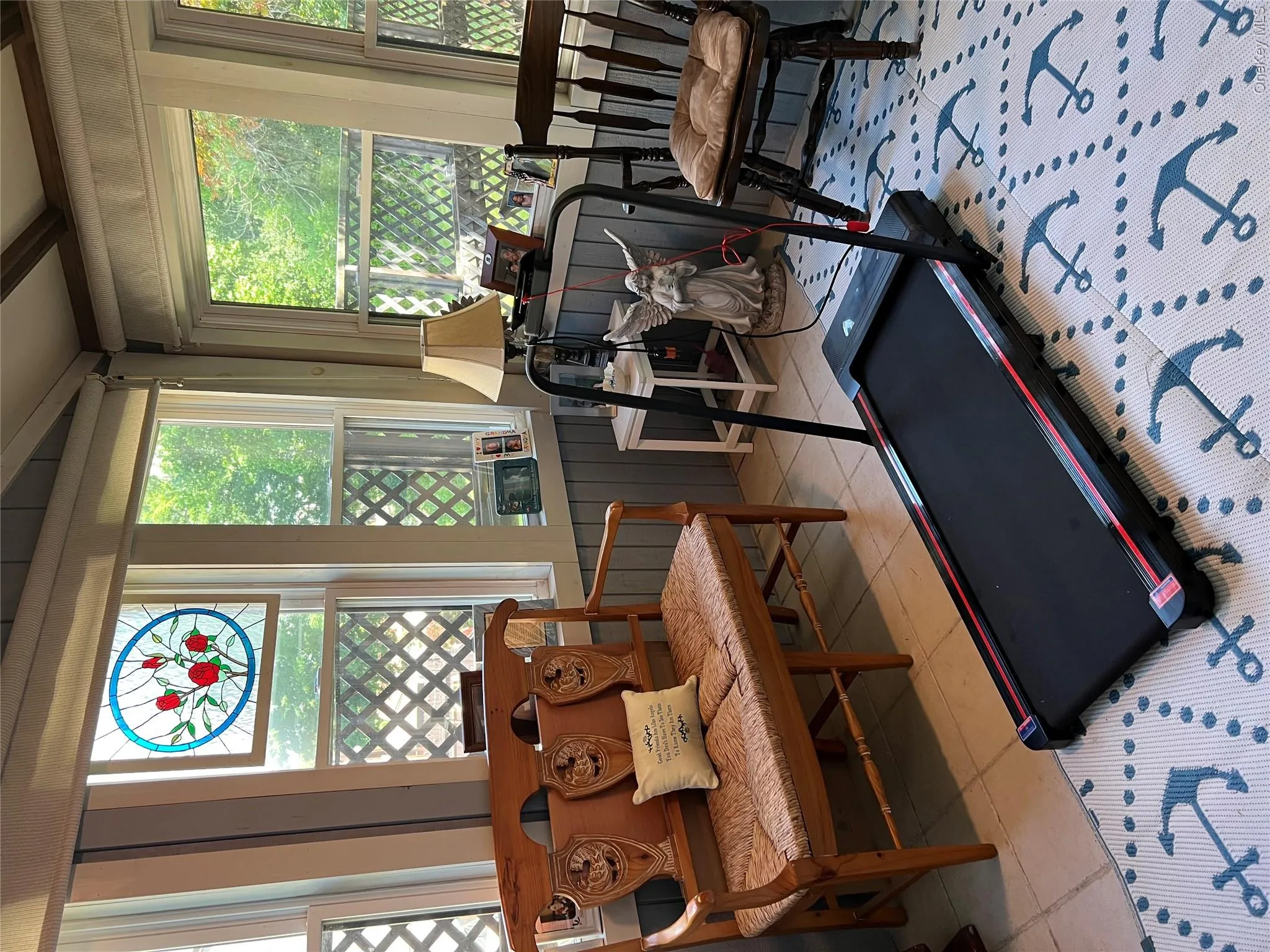 Sunroom featuring multiple windows, slatted wall paneling, a stained glass accent window, exposed wood ceiling beams, and light-toned tile flooring Sunroom featuring multiple windows, slatted wall paneling, a stained glass accent window, exposed wood ceiling beams, and light-toned tile flooring