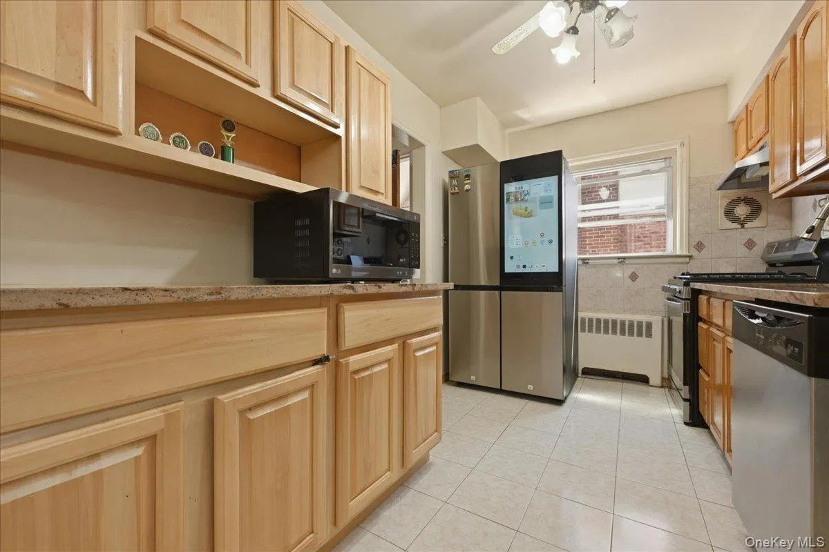 Kitchen featuring natural wood cabinetry, stone-finish countertops, stainless steel appliances, and tiled flooring Kitchen featuring natural wood cabinetry, stone-finish countertops, stainless steel appliances, and tiled flooring