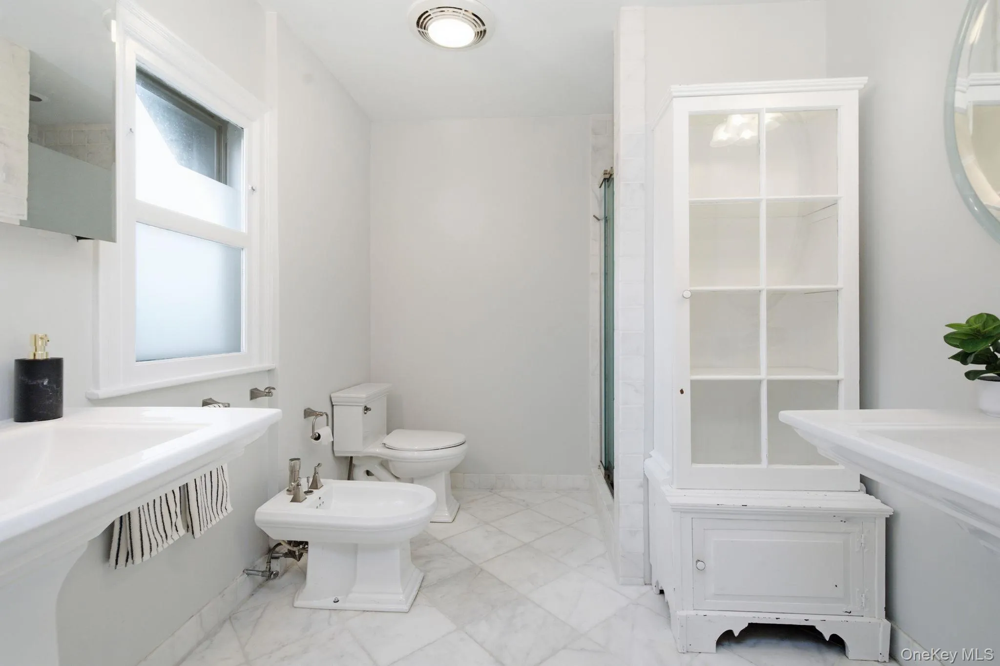 The marble bath features a glass door shower and classic pedestal sinks. The marble bath features a glass door shower and classic pedestal sinks.