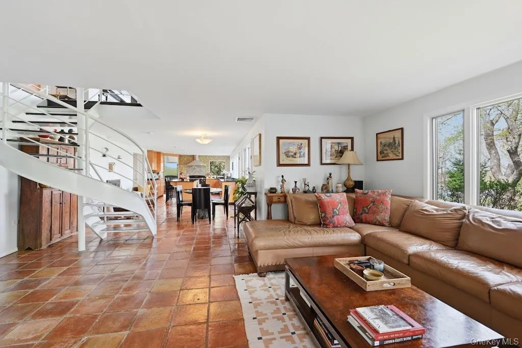 Open-concept living area featuring terracotta tile flooring, a white spiral staircase, and large windows Open-concept living area featuring terracotta tile flooring, a white spiral staircase, and large windows