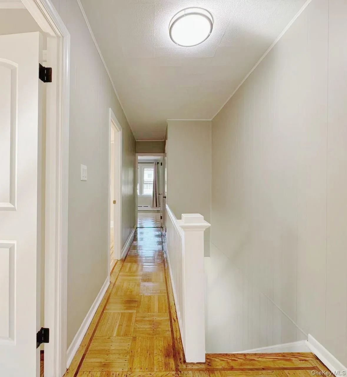 Hallway featuring light-toned walls, wood-finish parquet flooring, white trim, and a contemporary flush-mount ceiling light Hallway featuring light-toned walls, wood-finish parquet flooring, white trim, and a contemporary flush-mount ceiling light