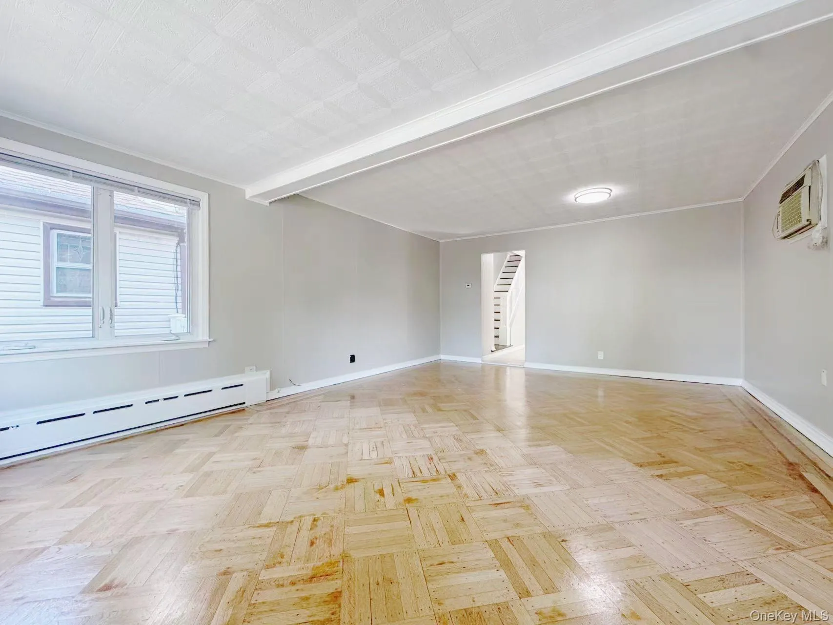 Spacious interior room featuring parquet wood flooring, light grey painted walls, and white baseboards Spacious interior room featuring parquet wood flooring, light grey painted walls, and white baseboards