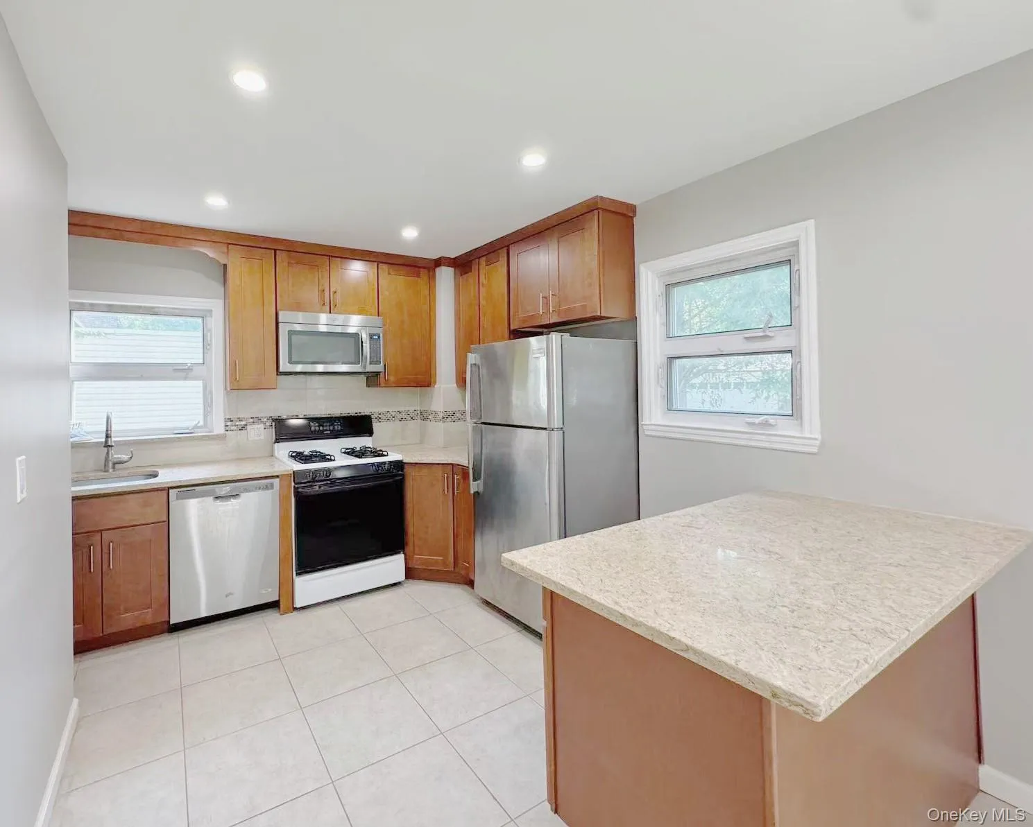 Kitchen featuring wood-finish cabinetry, stainless steel appliances, light-toned countertops, tile flooring, and recessed lighting Kitchen featuring wood-finish cabinetry, stainless steel appliances, light-toned countertops, tile flooring, and recessed lighting