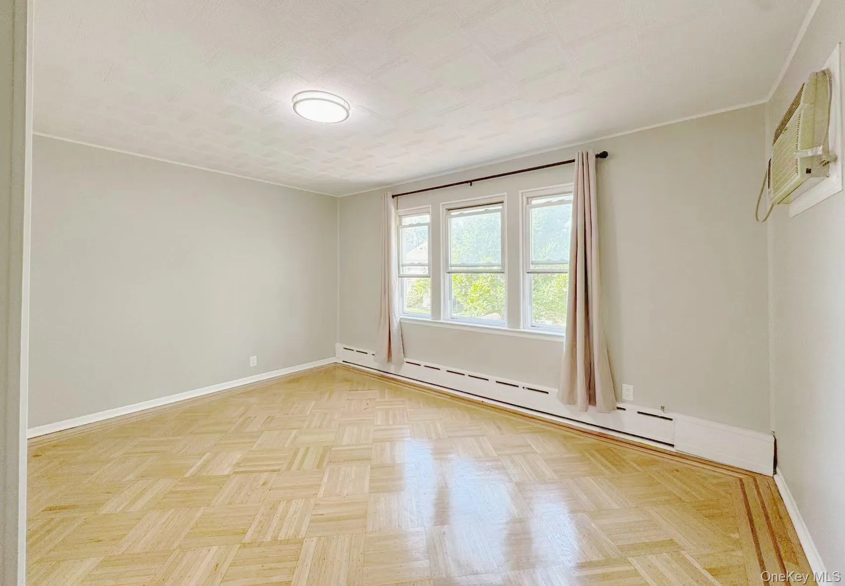 Room featuring parquet wood-finish flooring, light gray wall paint, and a triple window unit Room featuring parquet wood-finish flooring, light gray wall paint, and a triple window unit