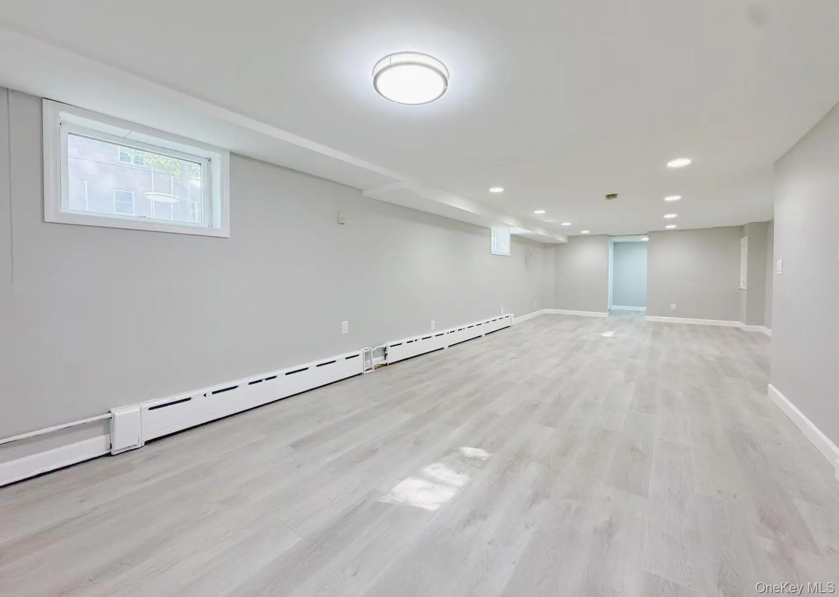 Spacious room featuring light wood-finish flooring, recessed lighting, baseboard heating, and a window with white trim Spacious room featuring light wood-finish flooring, recessed lighting, baseboard heating, and a window with white trim