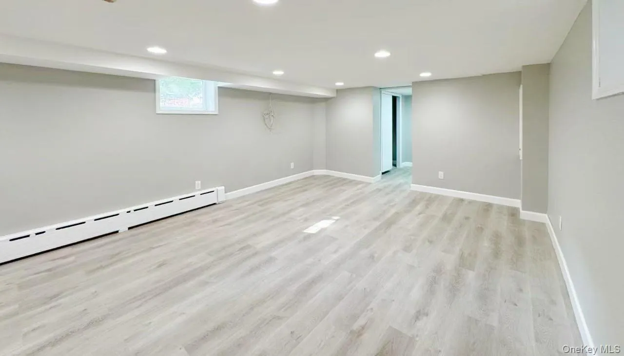 Spacious room featuring light wood-finish flooring, recessed lighting, neutral gray walls, and white baseboards Spacious room featuring light wood-finish flooring, recessed lighting, neutral gray walls, and white baseboards