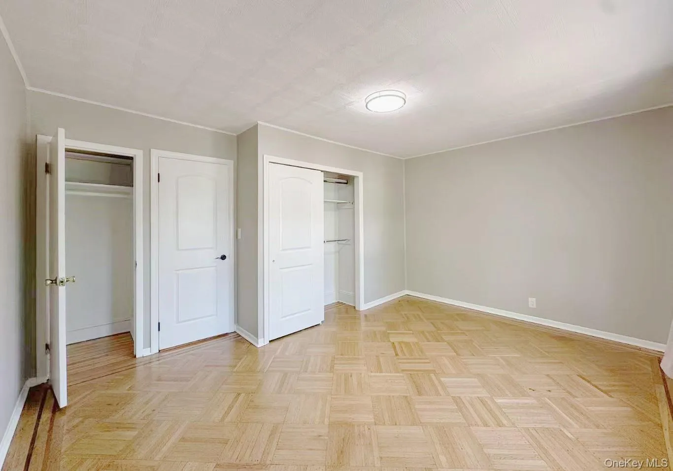 Interior room featuring parquet wood-finish flooring, light gray wall paint, and multiple white paneled doors Interior room featuring parquet wood-finish flooring, light gray wall paint, and multiple white paneled doors