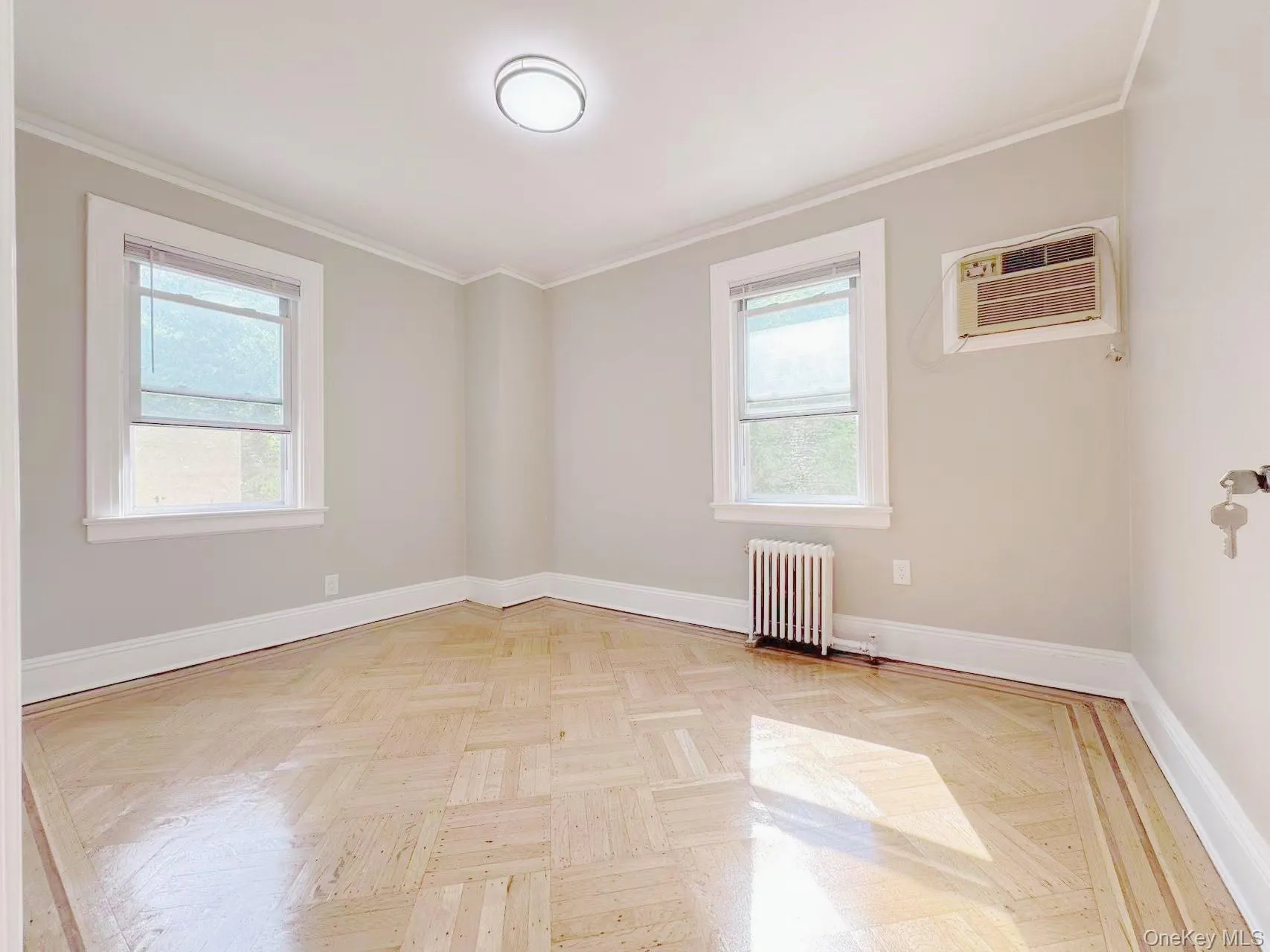 Parquet wood flooring with decorative border, two windows with white trim, wall-mounted air conditioning unit, and flush-mount ceiling light fixture Parquet wood flooring with decorative border, two windows with white trim, wall-mounted air conditioning unit, and flush-mount ceiling light fixture