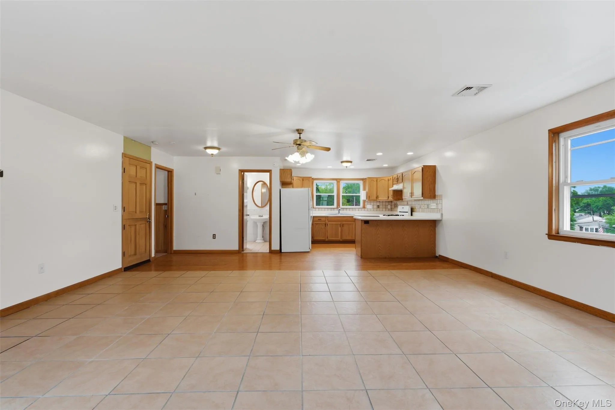 Expansive open-concept living area featuring light-toned square floor tiles, a kitchen with wood cabinetry Expansive open-concept living area featuring light-toned square floor tiles, a kitchen with wood cabinetry